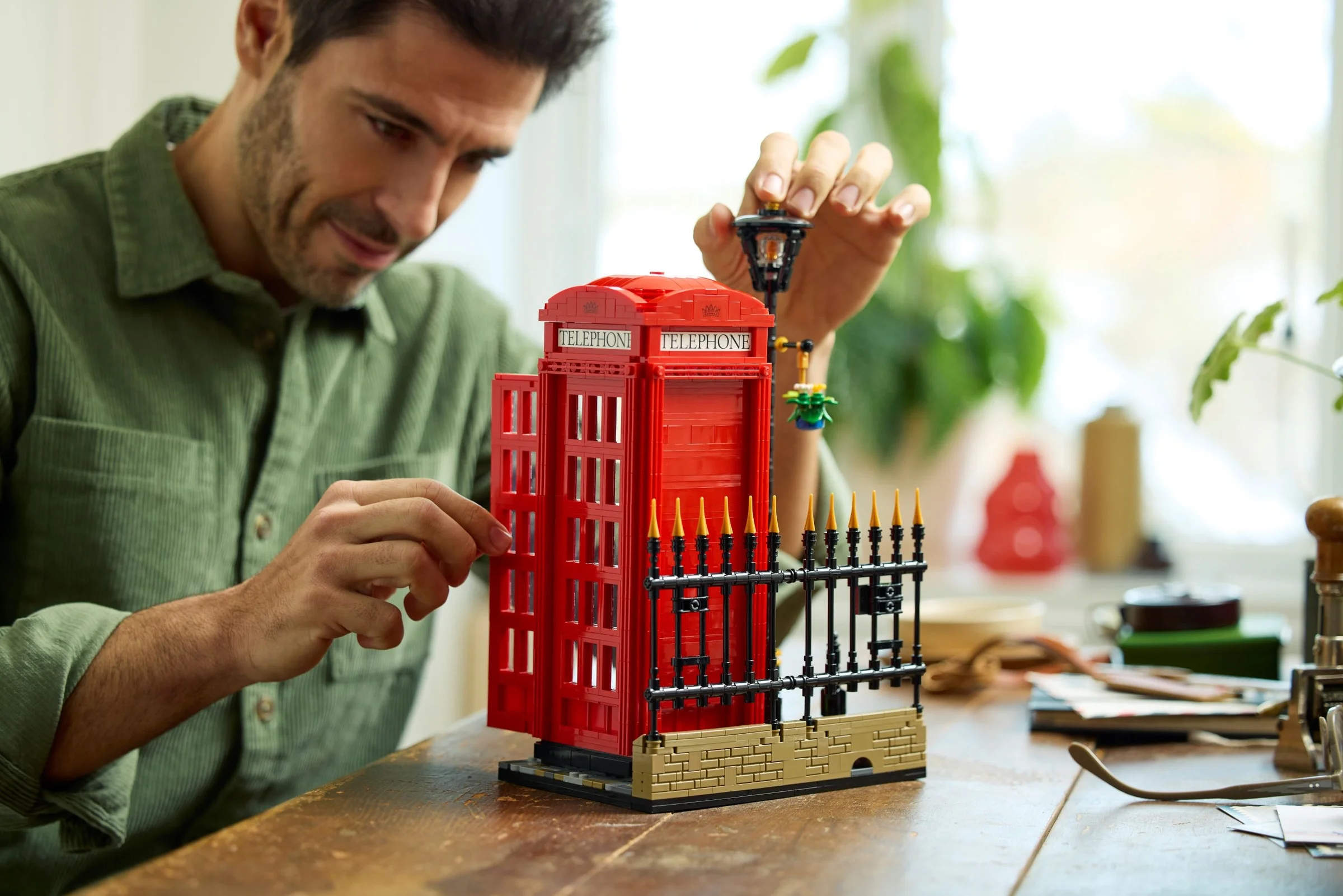 Bărbat asamblând cabina telefonică LEGO, detalii de construcție vizibile.