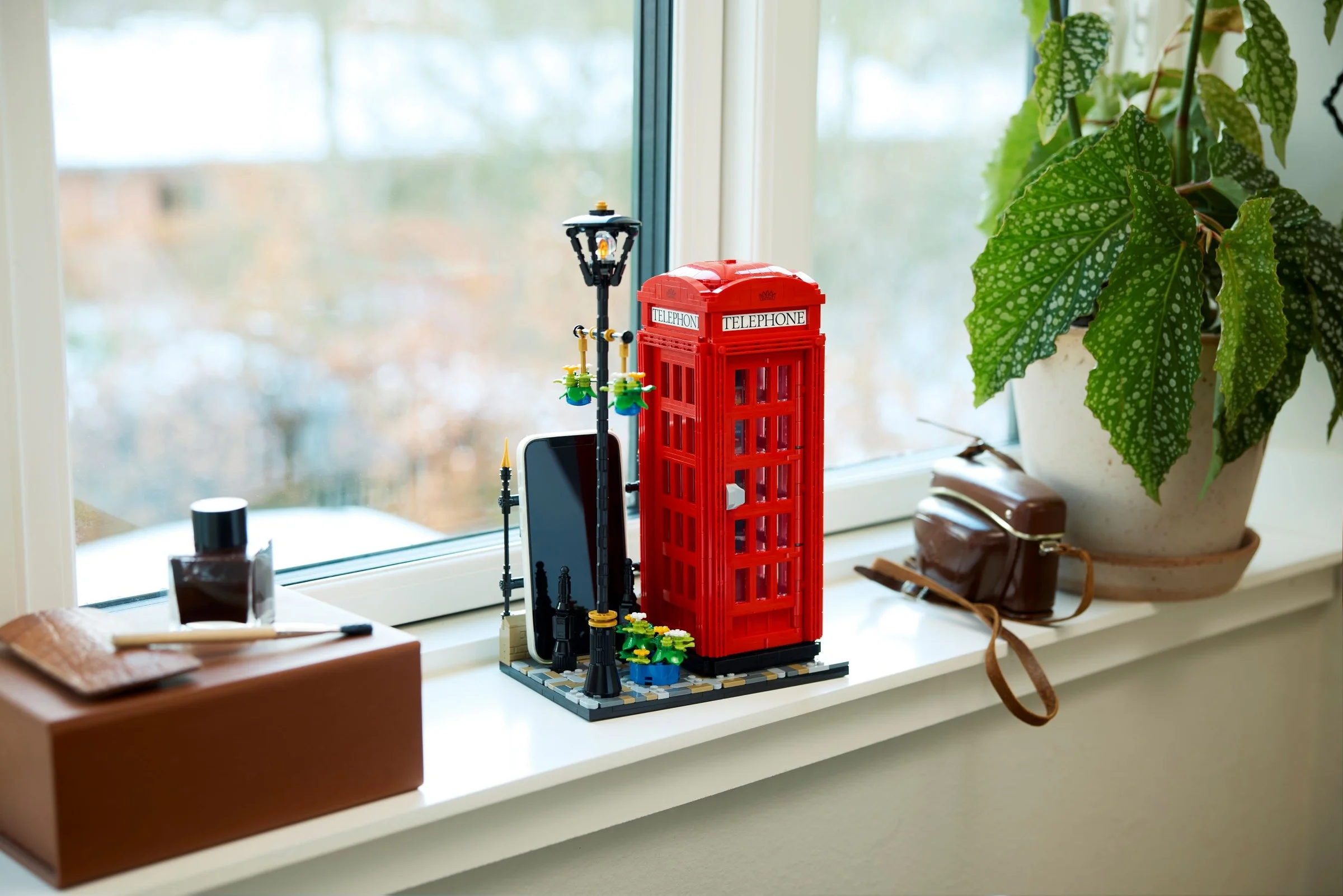 Telefonul public londonez LEGO roșu, lângă o lampă stradală, pe pervaz. Decorație interioară.