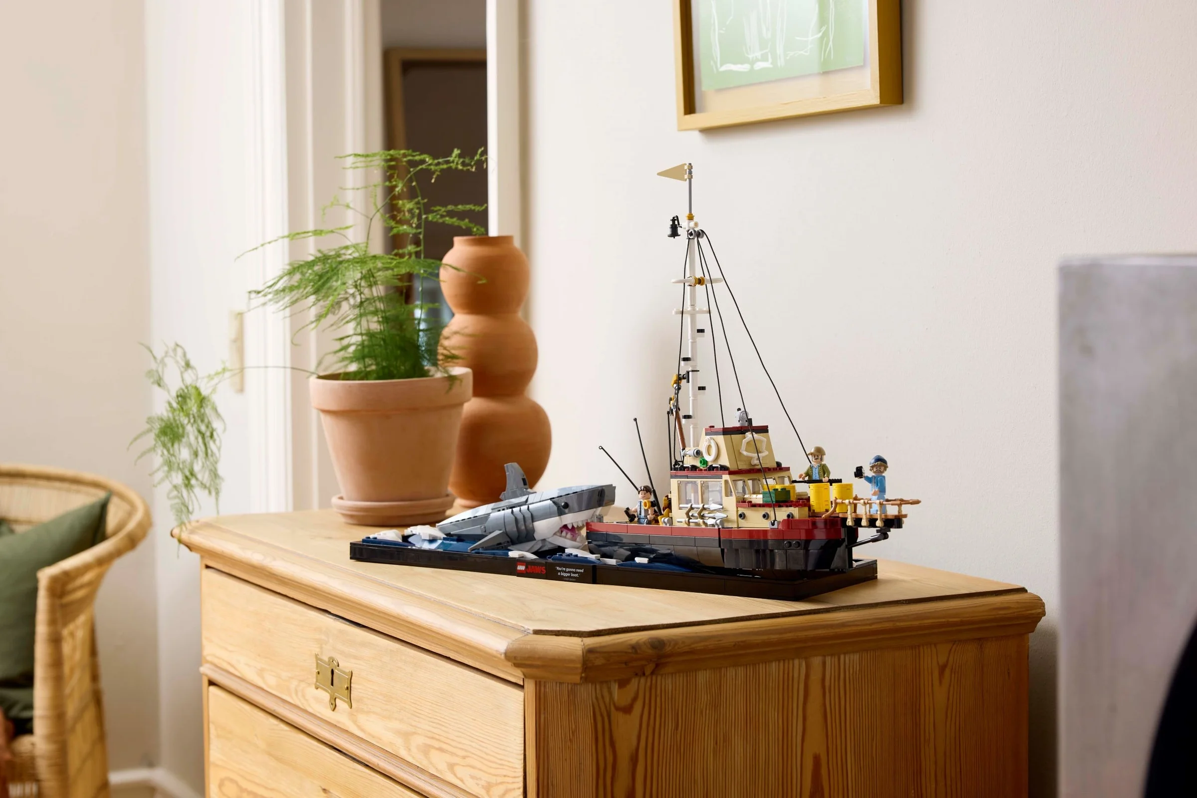 Modelul LEGO Jaws 21350 expus pe o comodă rustică, lângă o plantă și elemente decorative.