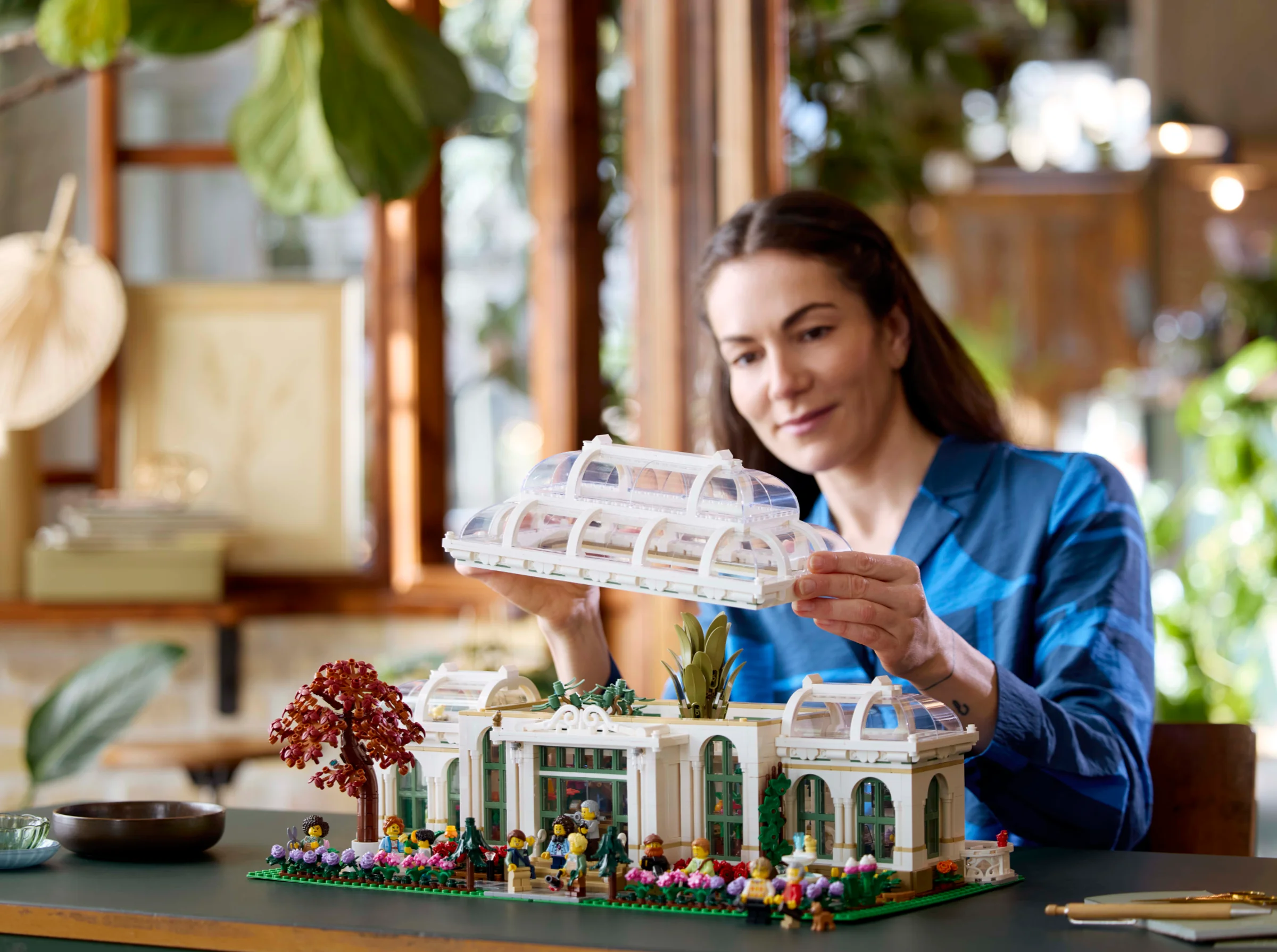 Femeie asamblează Grădina Botanică LEGO, adăugând secțiunea superioară clădirii principale.