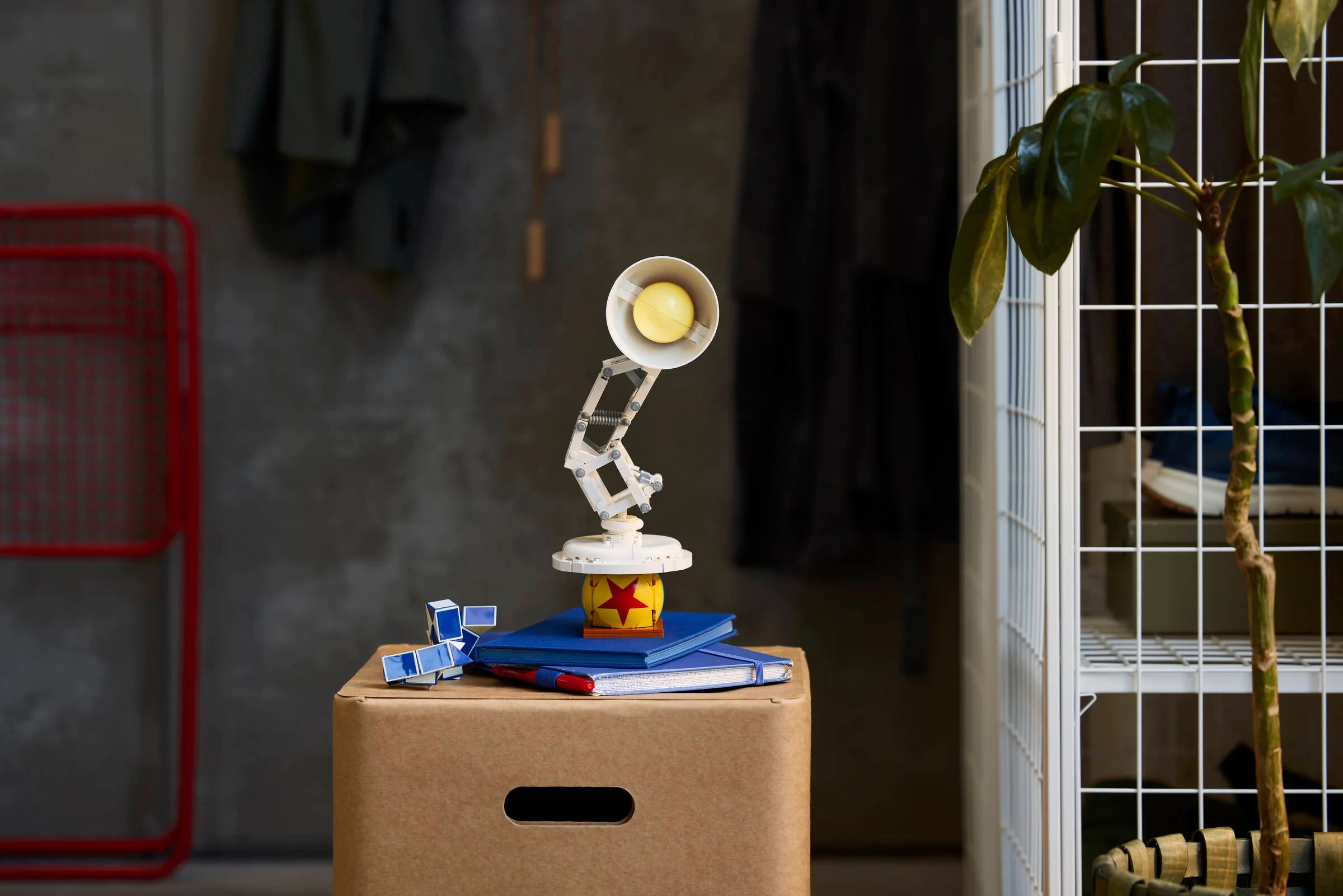 Lampa Luxo Jr. LEGO stă pe o grămadă de cărți, într-un decor ambient.