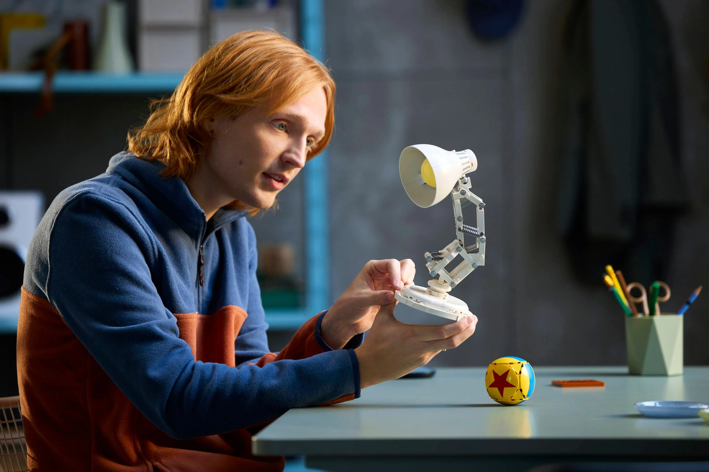 Un tânăr interacționează cu lampa Luxo Jr. din setul LEGO. Atitudine atentă.