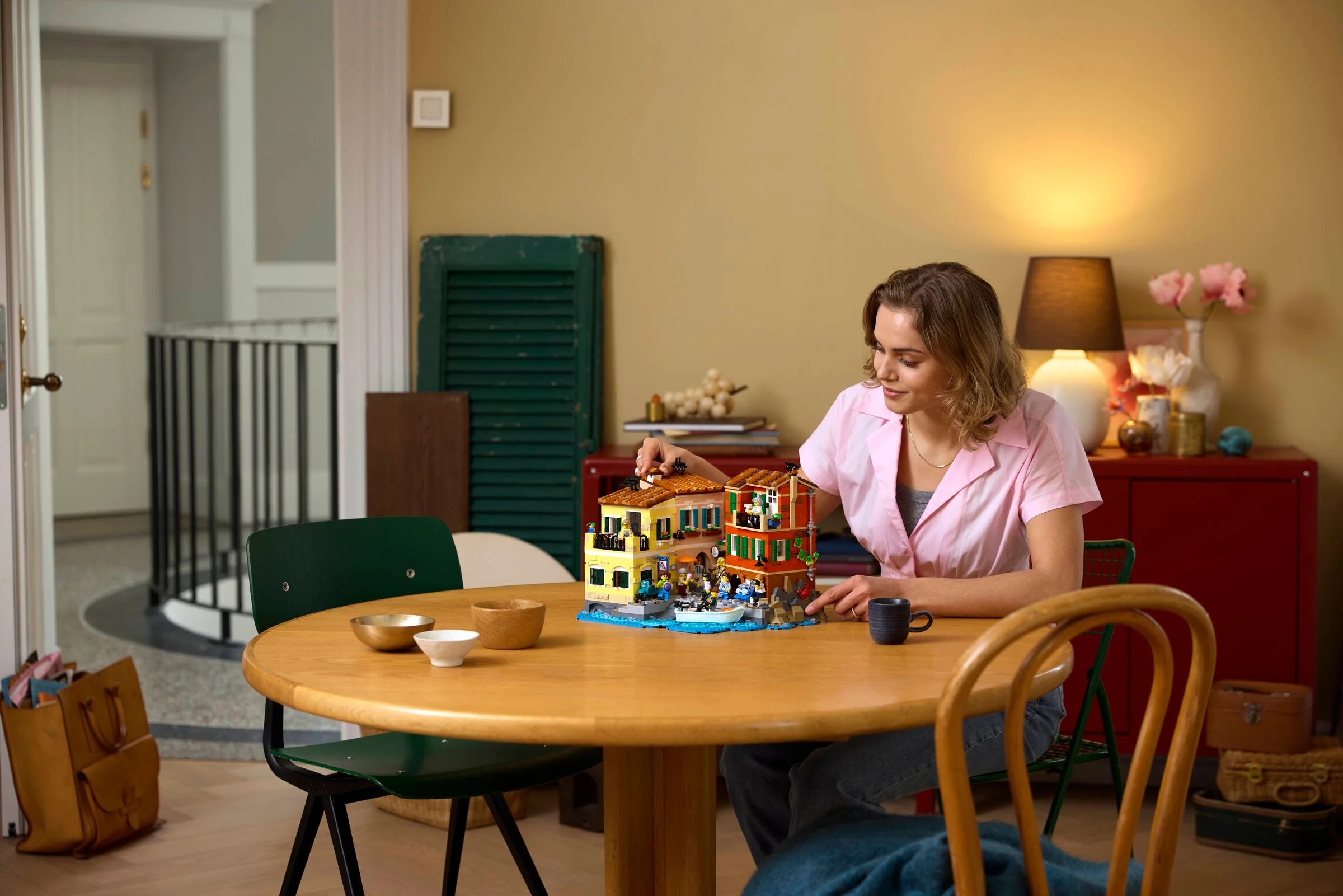 Femeie construind setul LEGO Italian Riviera pe o masă. Modelul este detaliat, cu minifigurine.