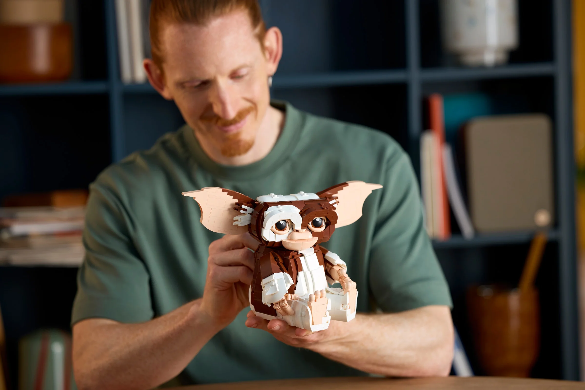 Un bărbat zâmbește privind modelul LEGO Gizmo finalizat, pe care îl ține în mâini.