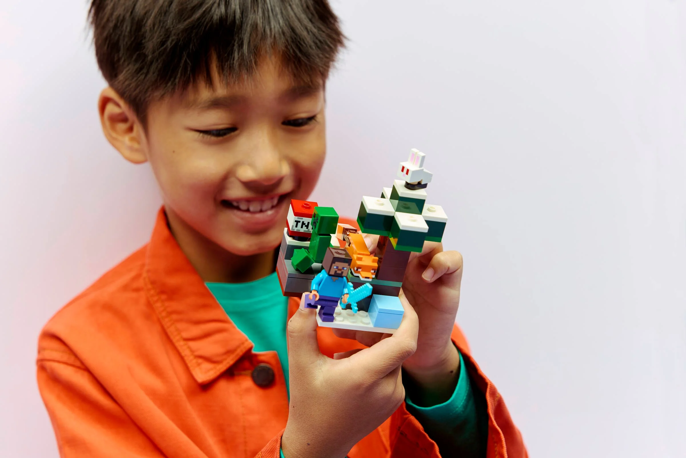 Un băiat zâmbitor admiră setul LEGO Minecraft Aventura în Taiga a lui Steve (21583).