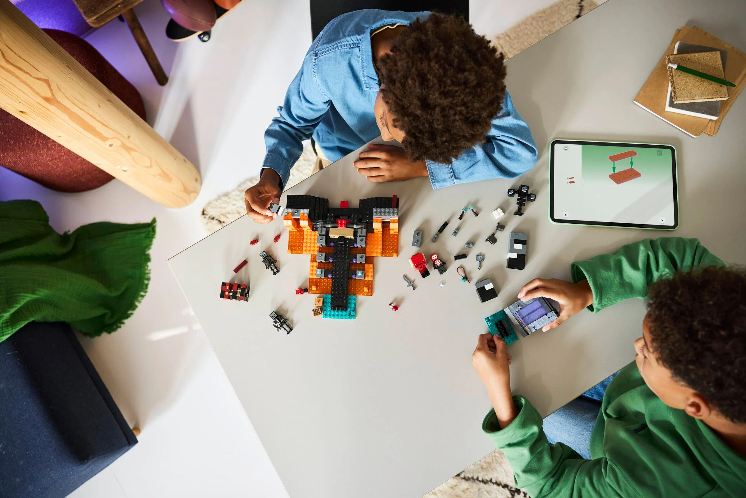 Copii asamblând setul LEGO Minecraft 21590, având instrucțiuni pe tabletă.