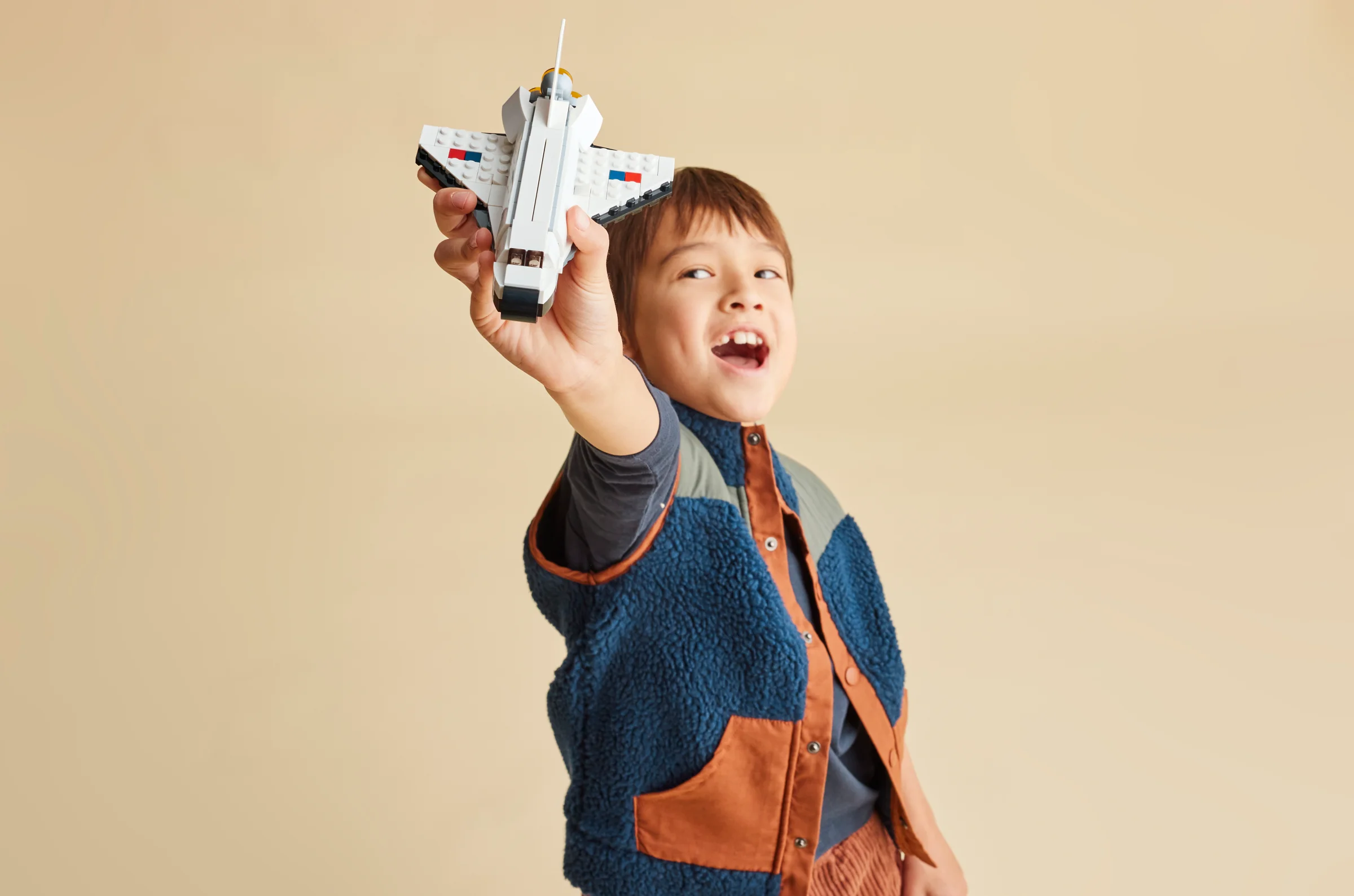 Copil zâmbitor ținând naveta spațială LEGO, sugerând joacă și creativitate.