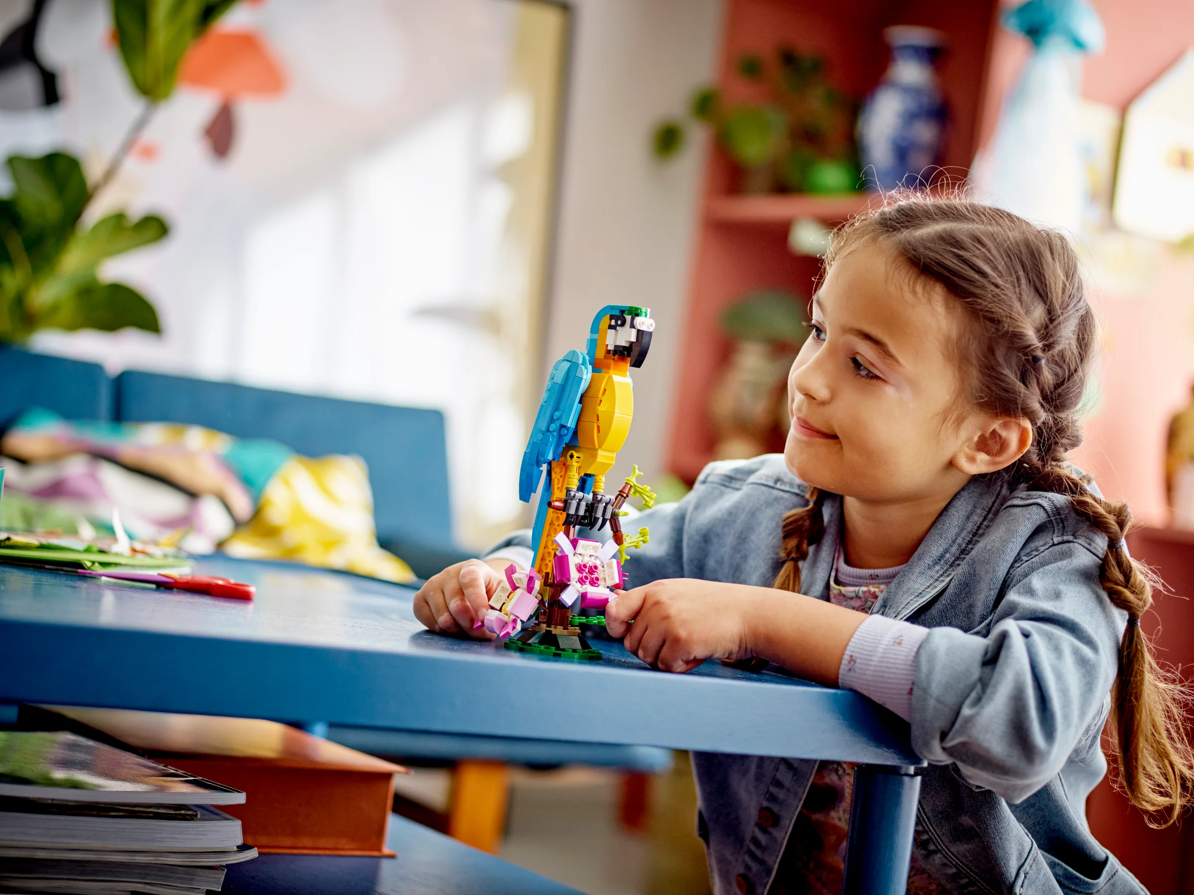 Fetiță admirând papagalul exotic LEGO Creator 31136, așezat pe o ramură cu flori roz.