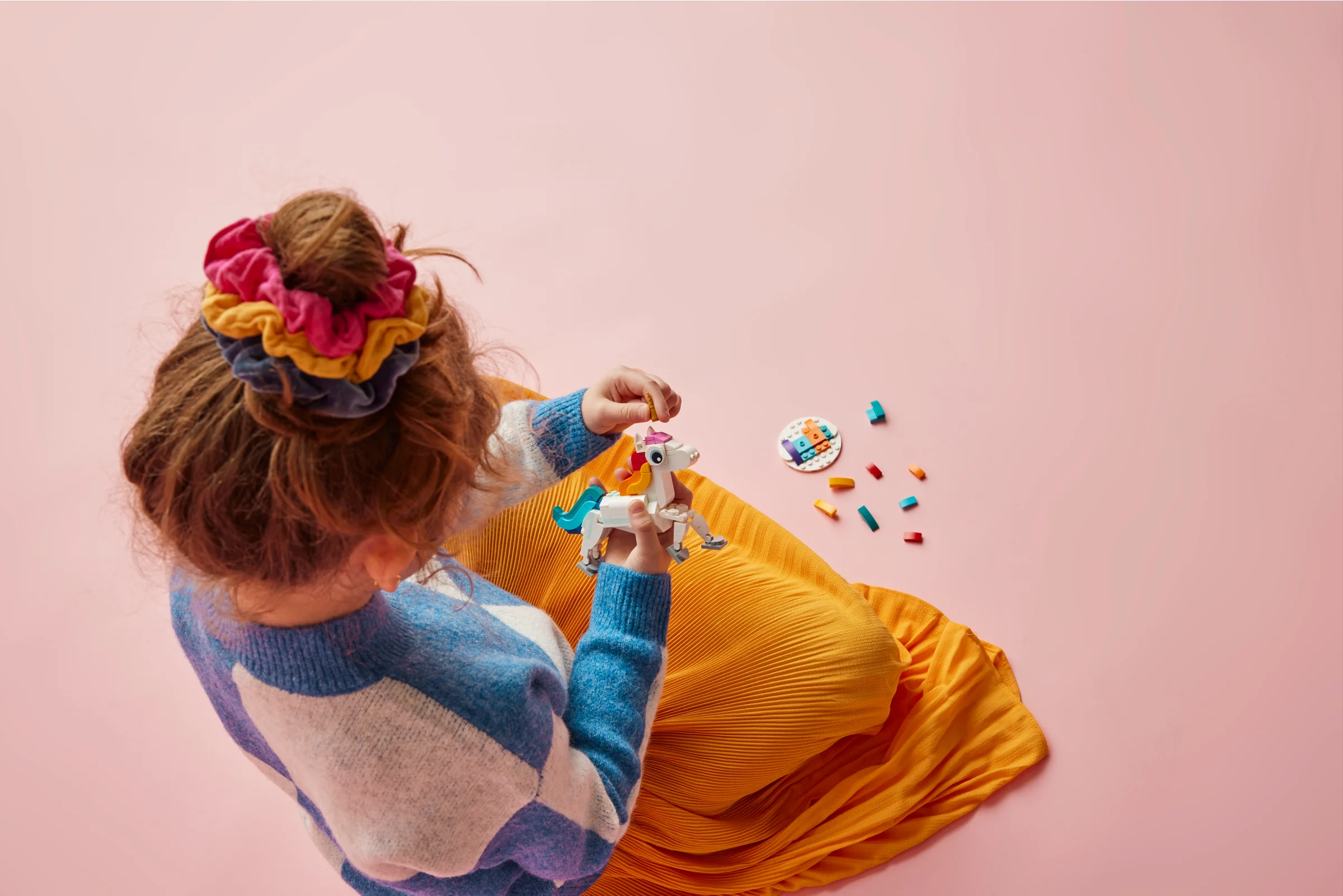 Fetiță construind unicornul magic LEGO. Imagine de sus, fundal roz.