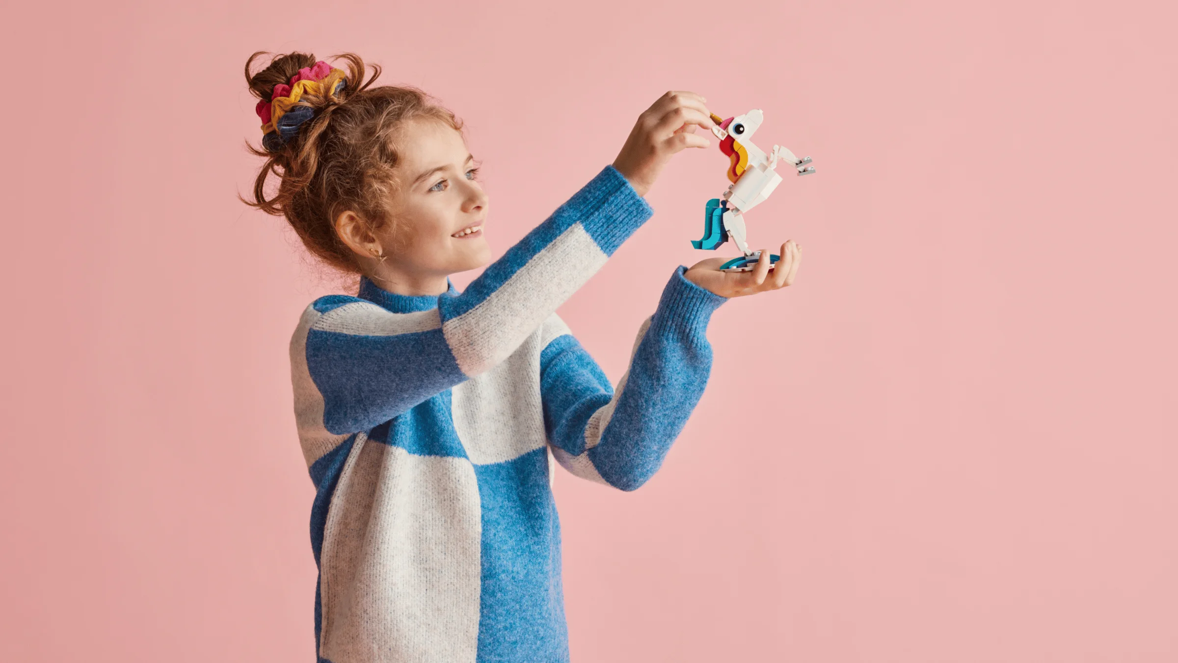 O fetiță ține un unicorn LEGO Creator 31140. Zâmbește și admiră modelul.