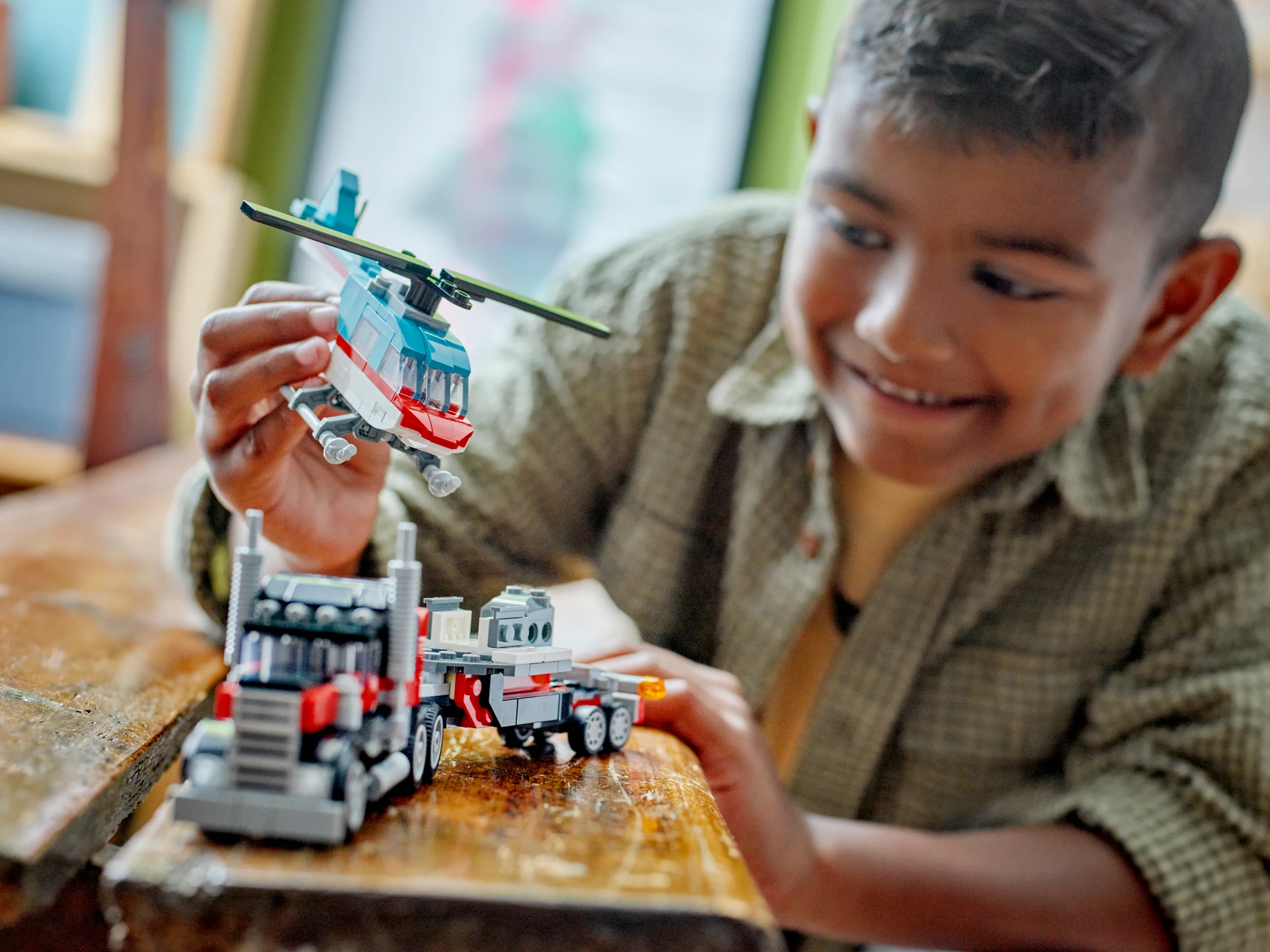 Băiat zâmbitor se joacă cu camionul și elicopterul LEGO din setul 31146.