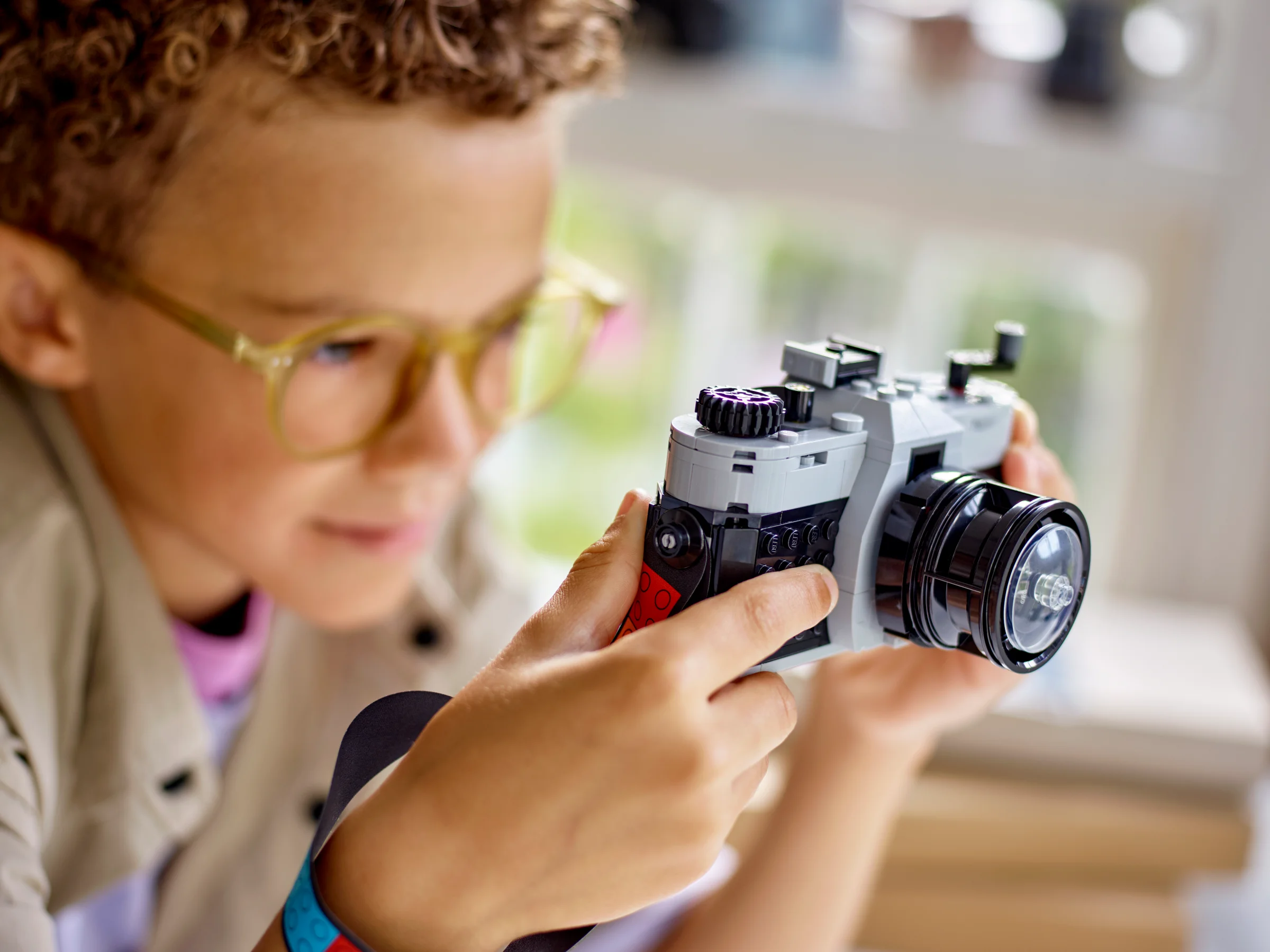 Un copil ține camera retro LEGO, examinând detaliile construcției. Focalizare pe cameră și mâini.