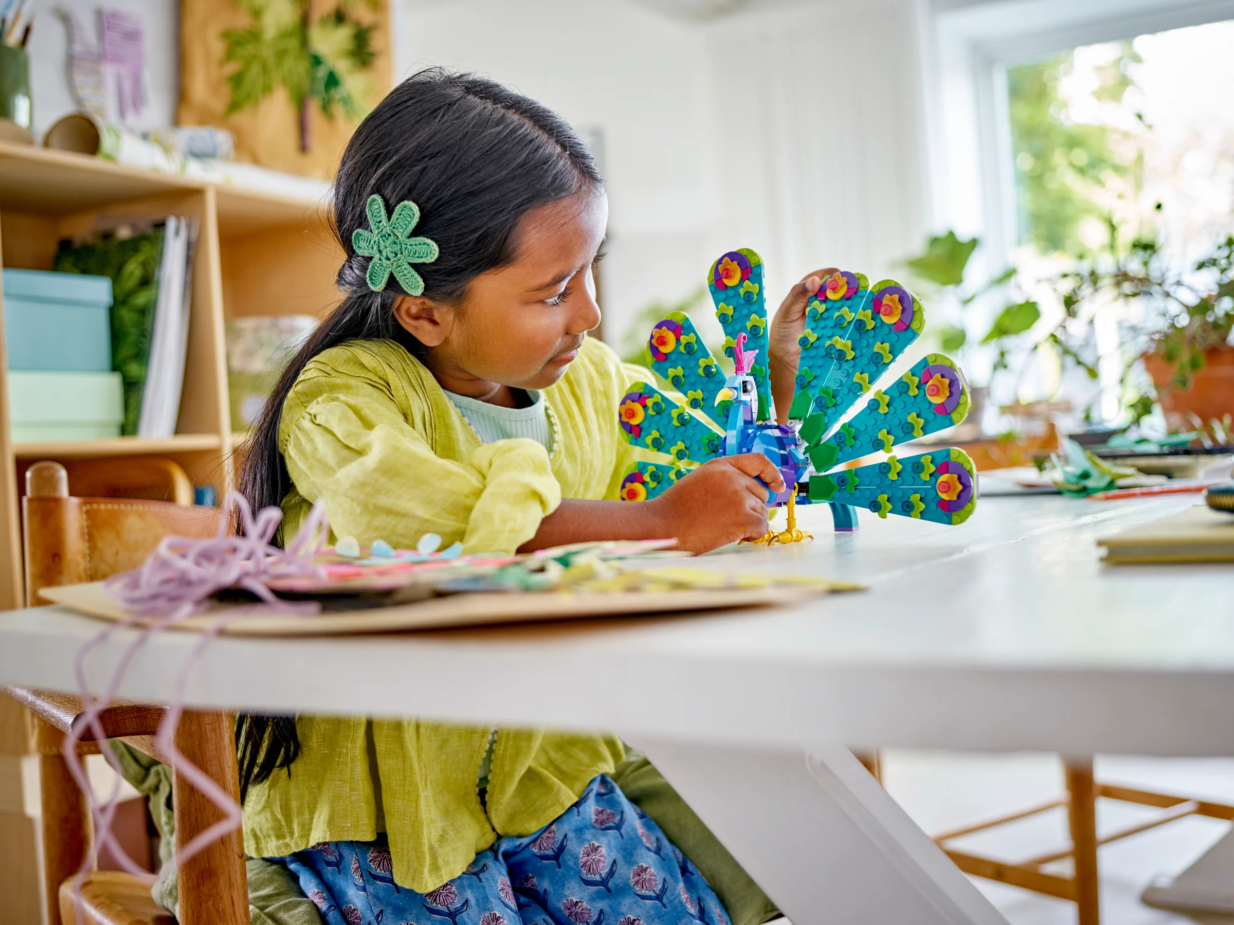 Fetiță construind un păun LEGO viu colorat, cu detalii florale distincte.