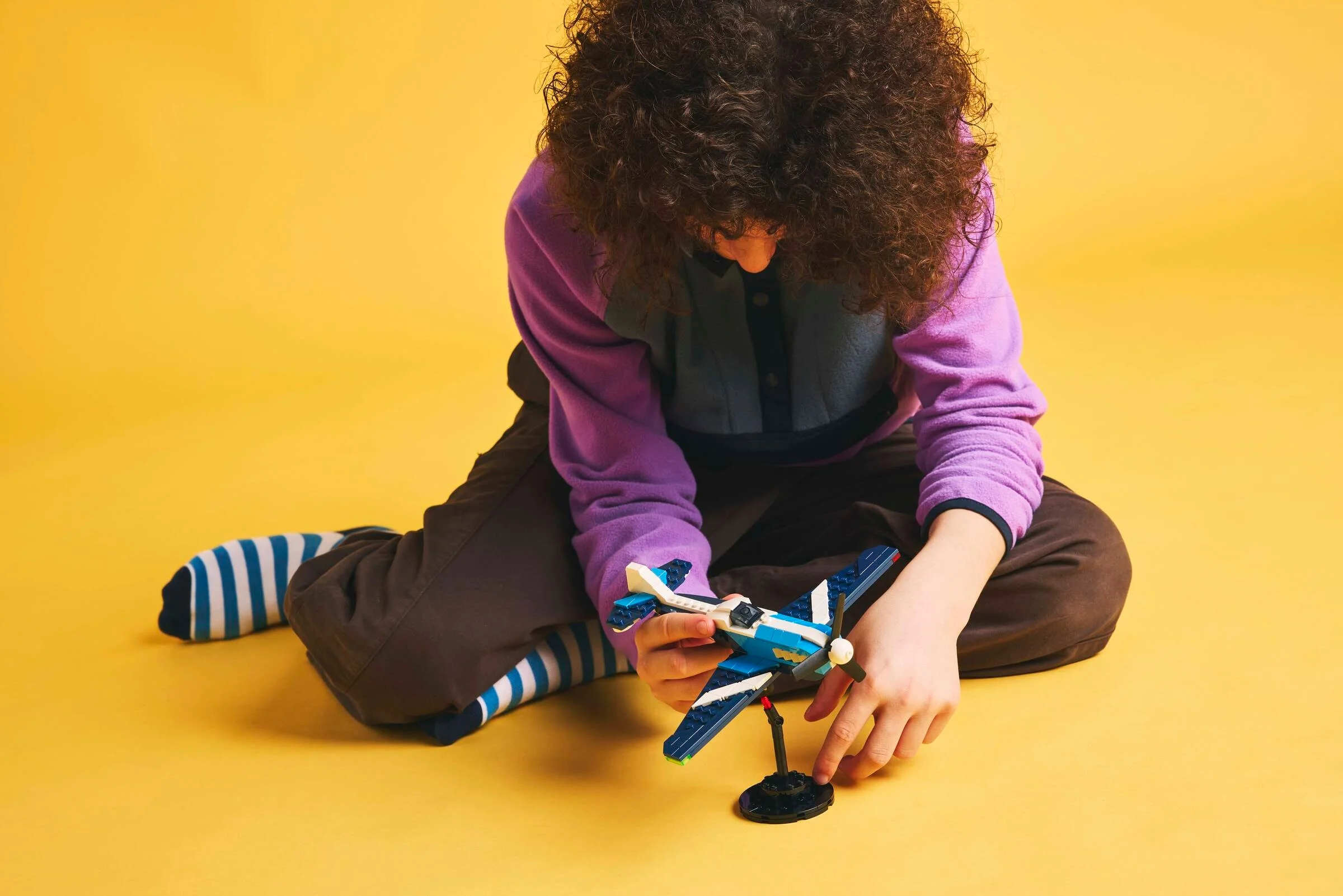 Un copil se joacă cu avionul de curse LEGO Creator 31160, pe un fundal galben.