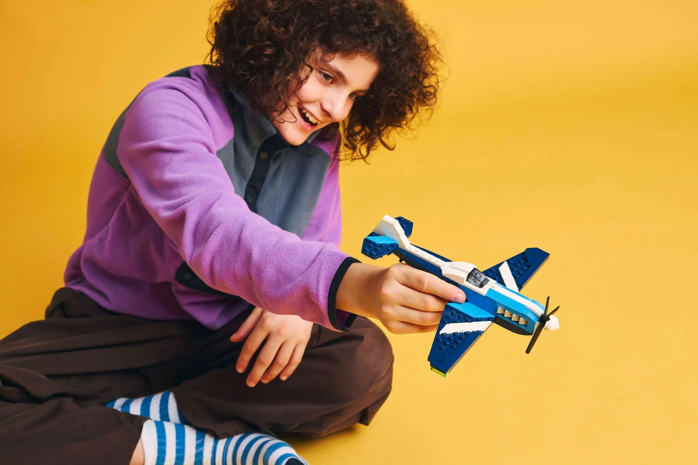 Un copil zâmbitor ține avionul de curse LEGO 31160, pe un fundal galben.