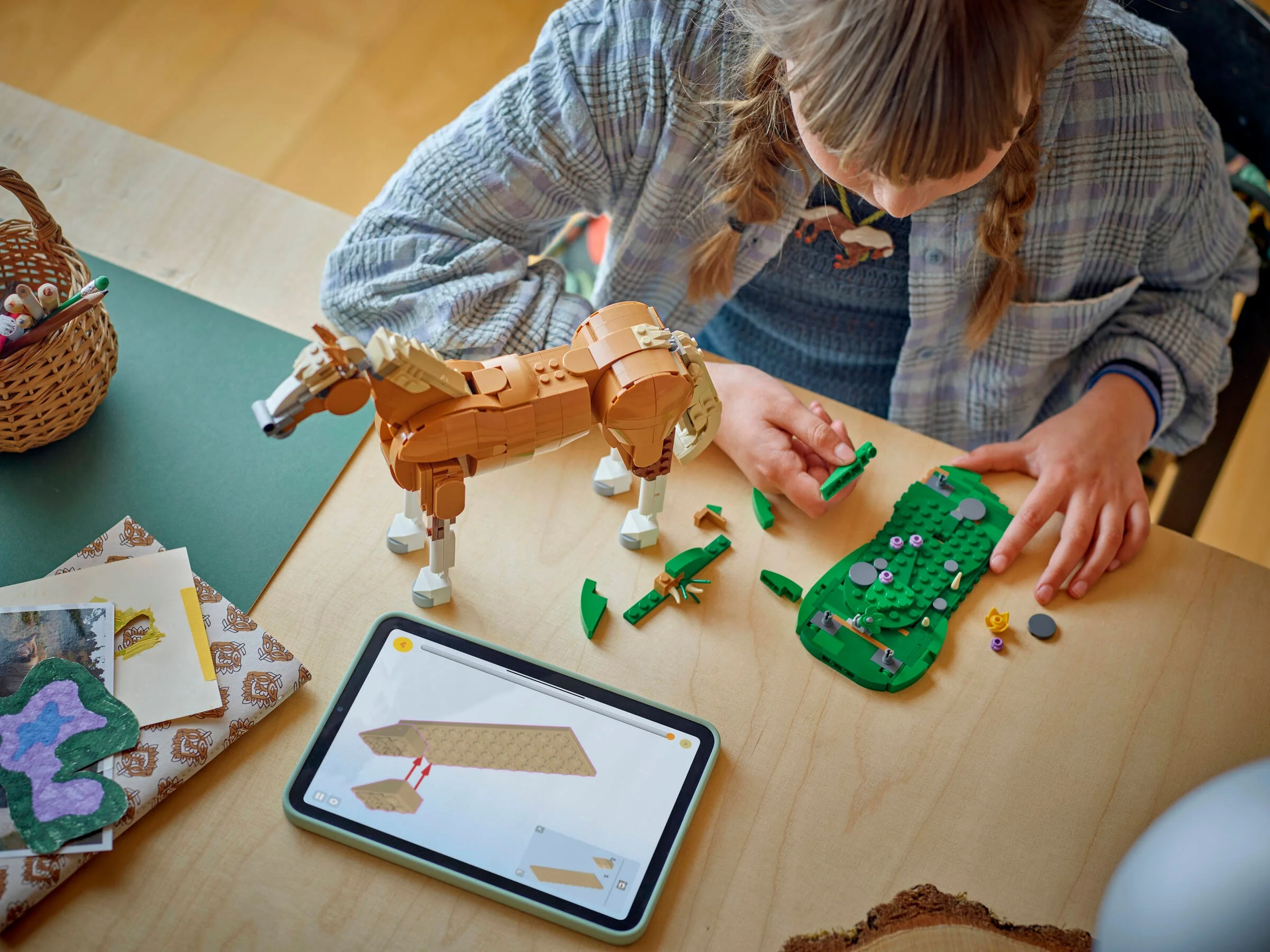 Fetiță construind calul LEGO 31166, urmărind instrucțiunile pe tabletă. Scenă creativă.