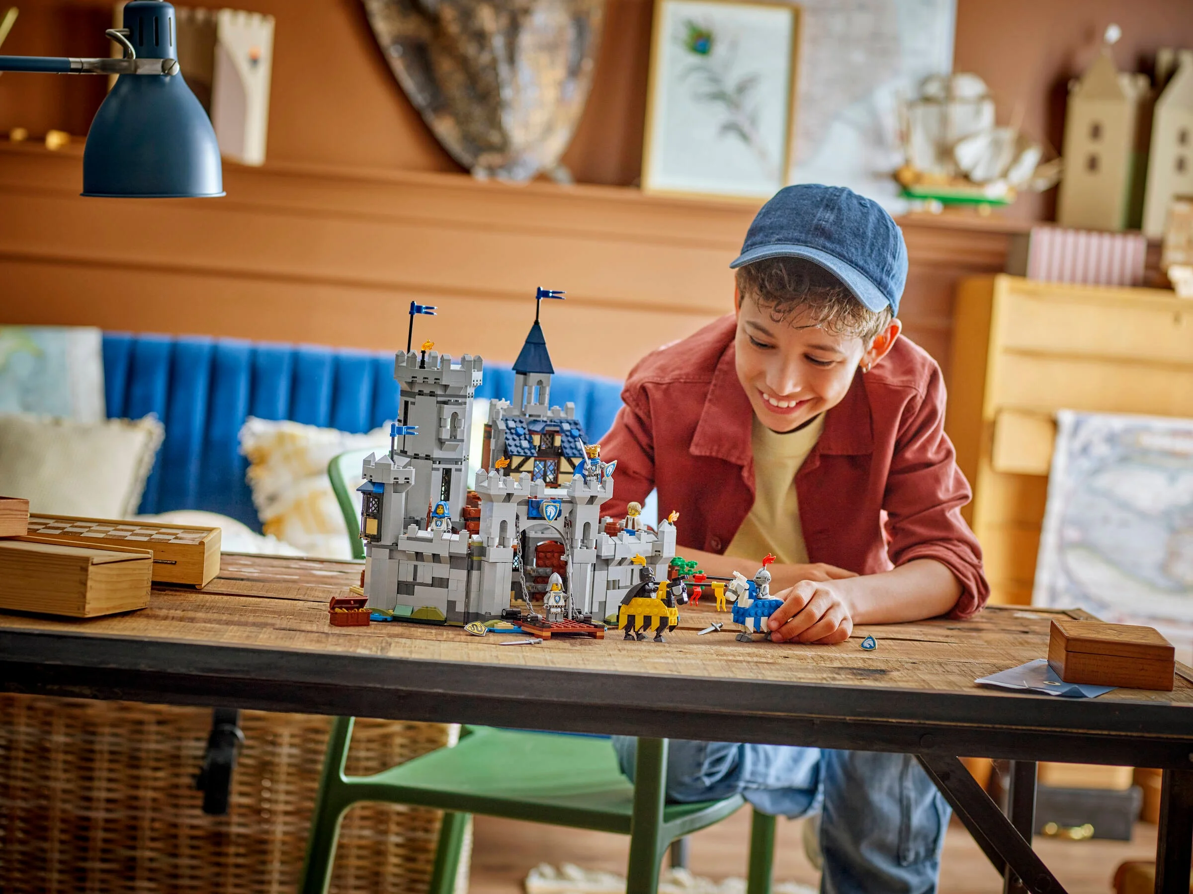 Copil zâmbind jucându-se cu castelul medieval LEGO 31168 pe o masă rustică.