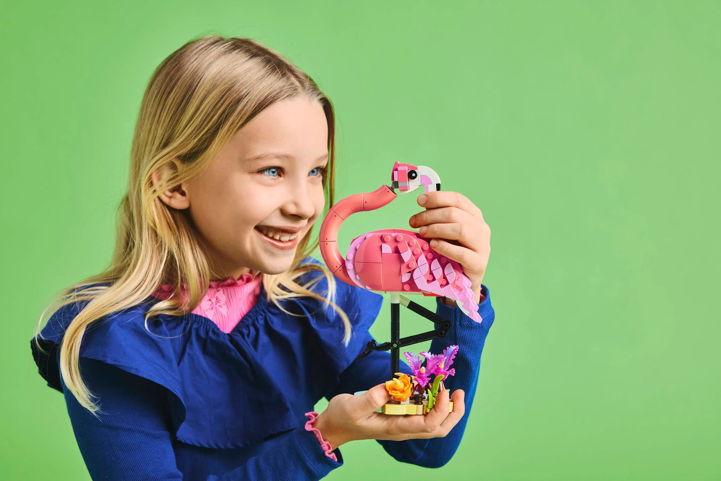Fetiță zâmbind cu flamingo roz LEGO în mâini. Aspect vesel.