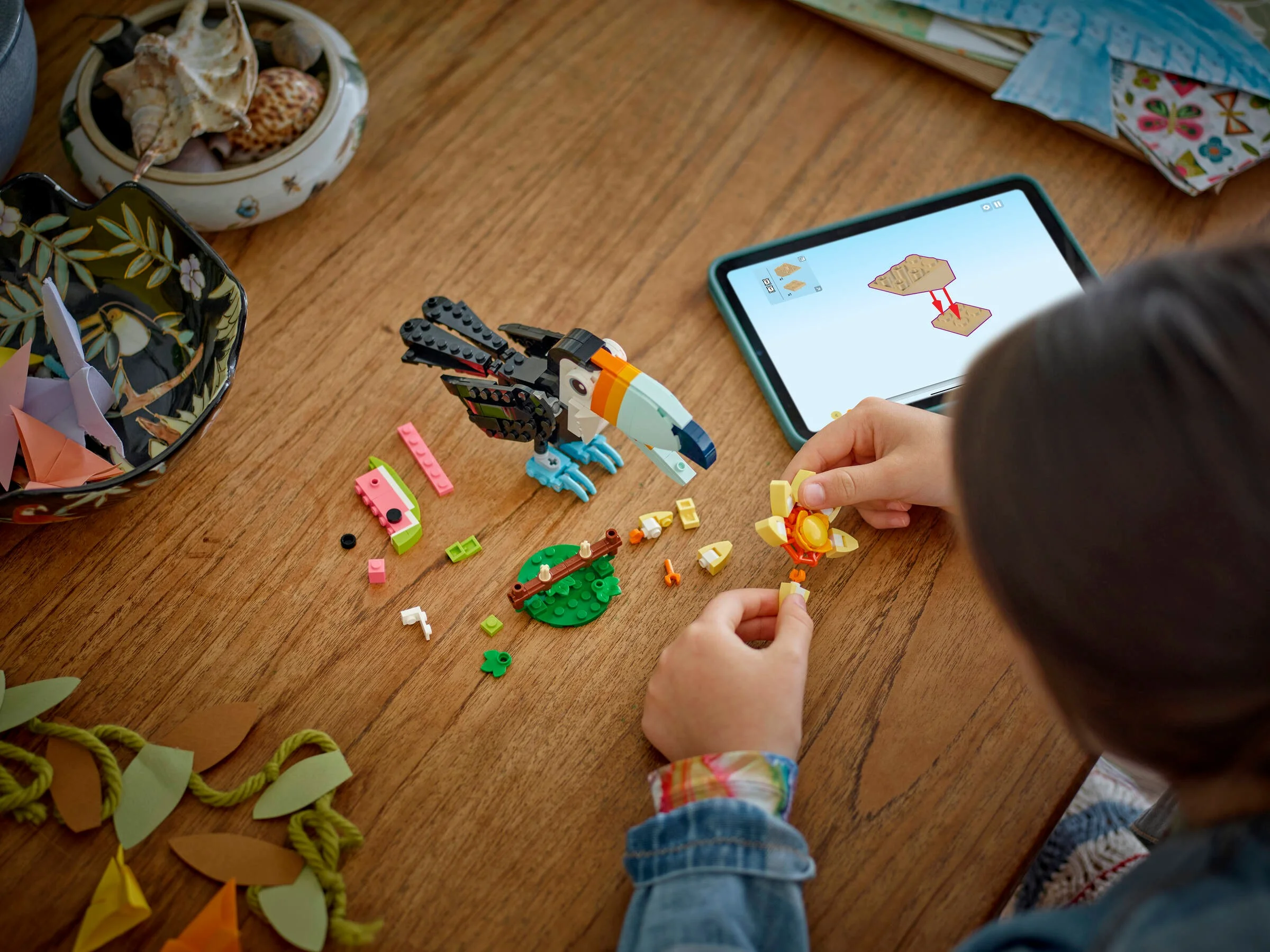 Copil construind setul LEGO Toucan Tropical (31173) după instrucțiuni de pe tabletă.
