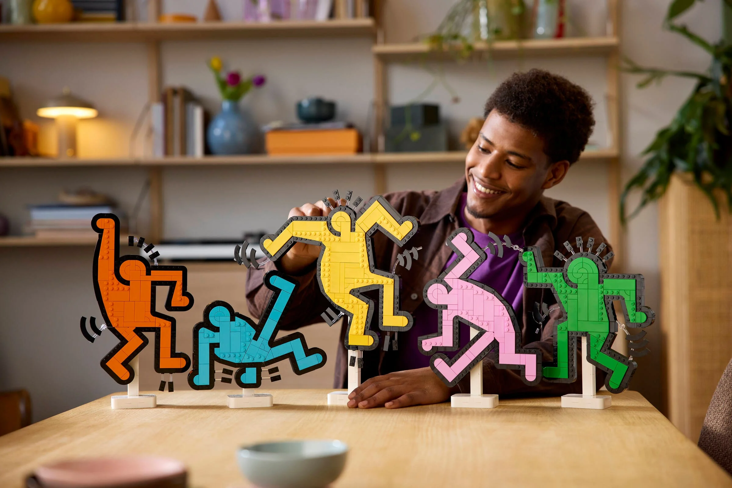 Personă interacționând cu setul LEGO Keith Haring. Figurinele sunt viu colorate.