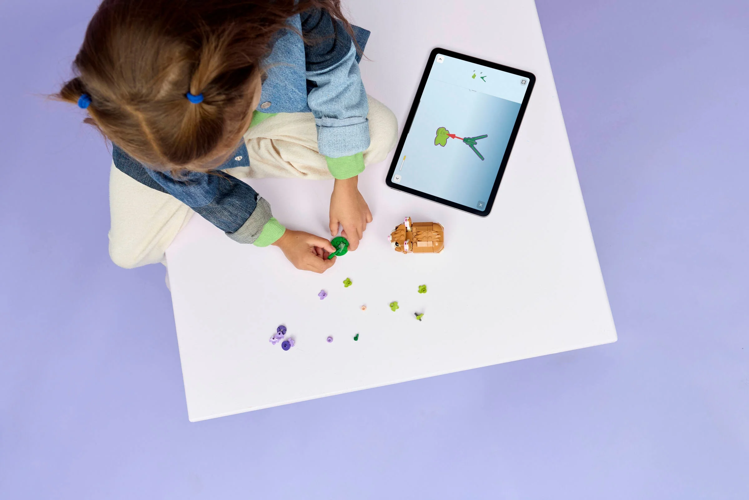 O fetiță construiește hamsterul LEGO cu ajutorul instrucțiunilor digitale pe tabletă.
