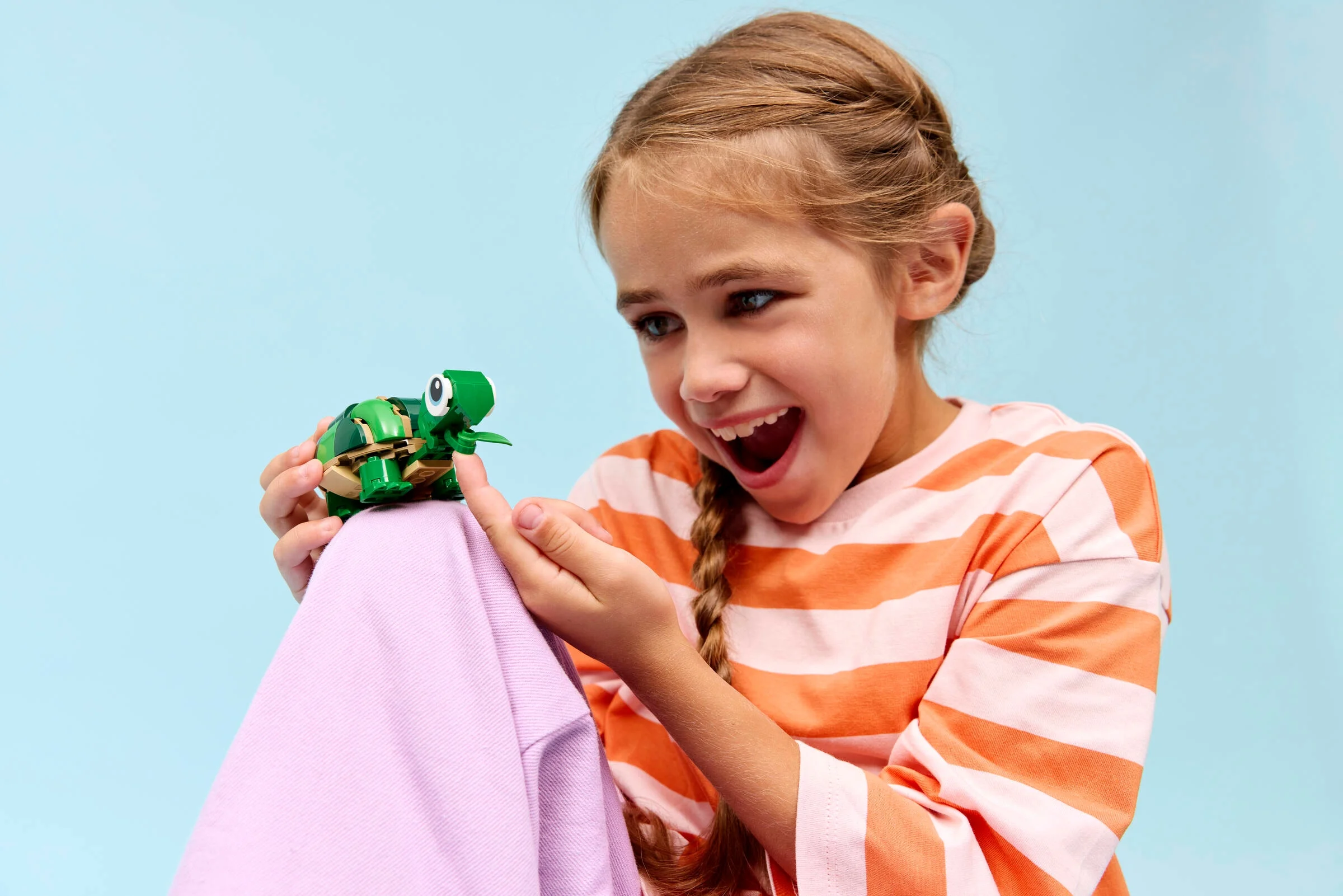 Fetiță entuziasmată admirând broasca țestoasă LEGO Creator. Model detaliat, atractiv pentru copii.