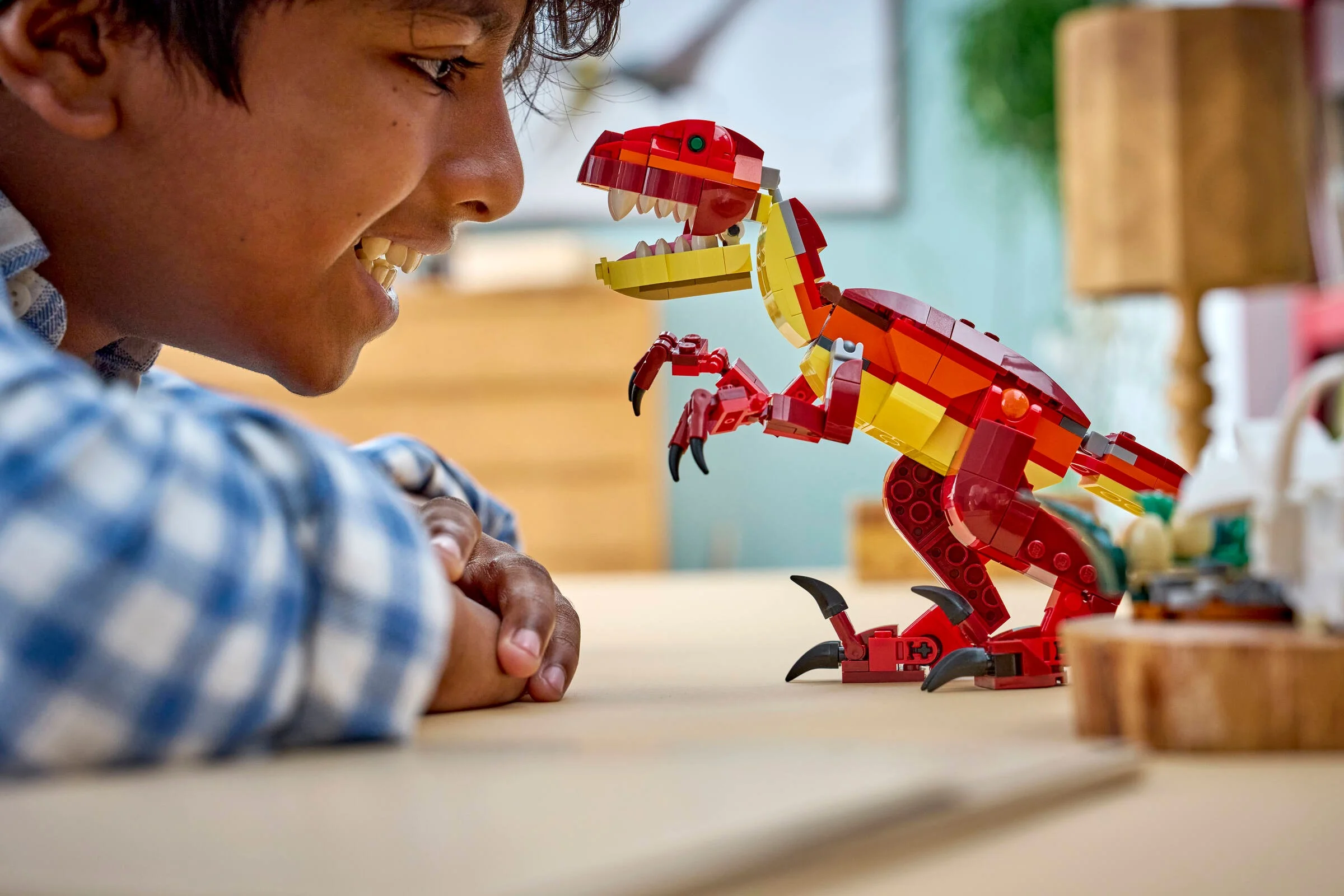 Băiat entuziasmat admirând dinozaurul LEGO roșu și galben, detaliu. Dinozaurul pare fioros.