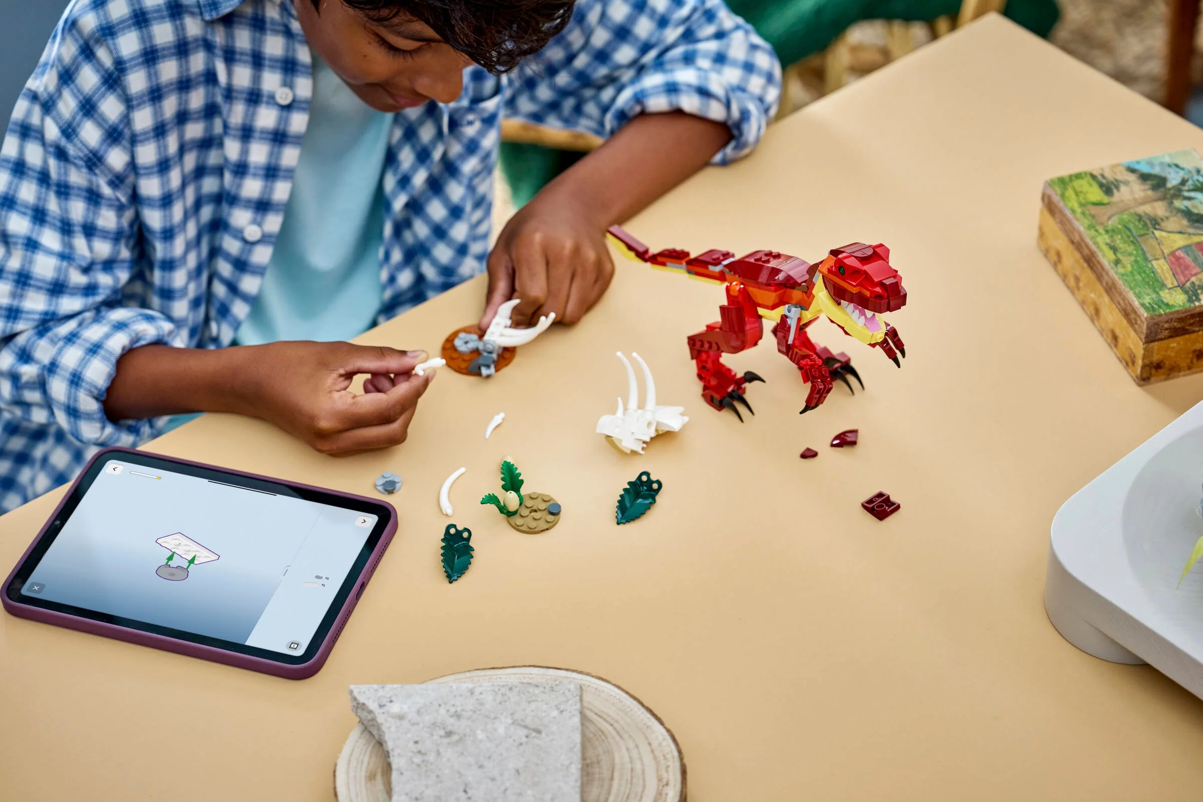Copil construind un dinozaur LEGO. Se folosește de instrucțiuni digitale pe tabletă.
