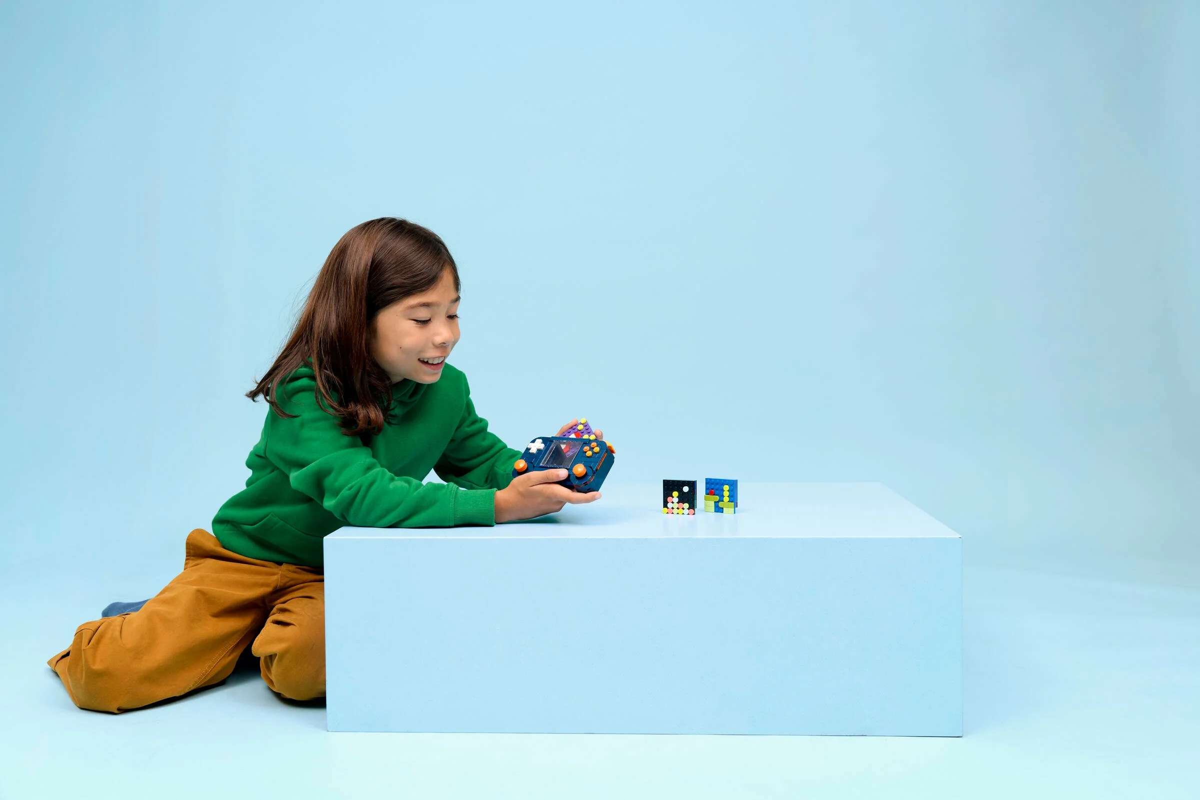 O fată zâmbind se joacă cu consola retro LEGO® Creator 31380. Consola și două mini-jocuri sunt pe o masă.