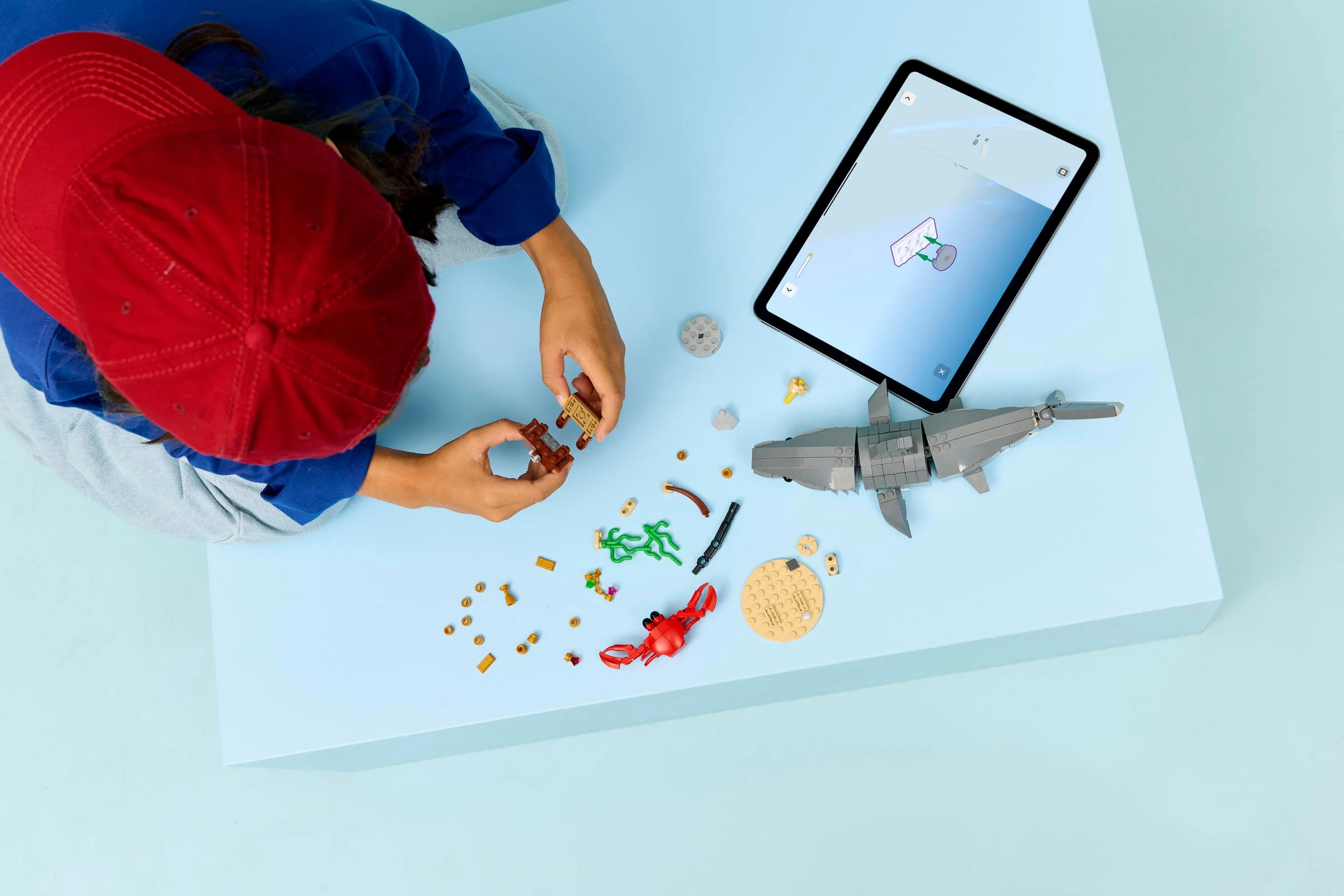 Copil construind setul LEGO 31381, cu rechin, crab și cufăr, folosind instrucțiuni digitale.
