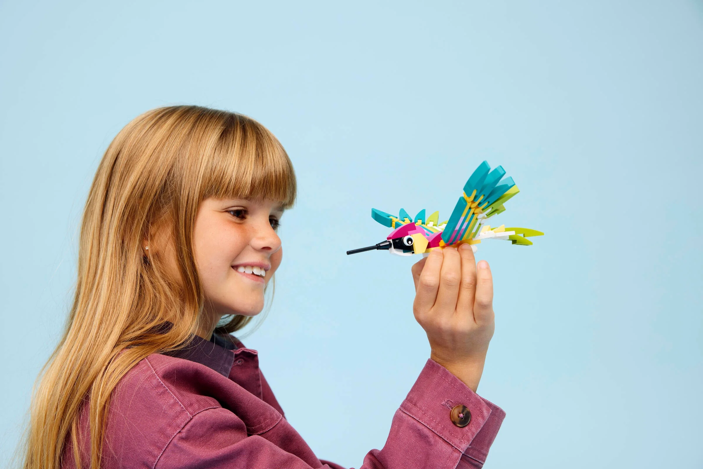 Fetiță zâmbitoare admirând colibriul colorat LEGO Creator. Jucărie creativă și distractivă.