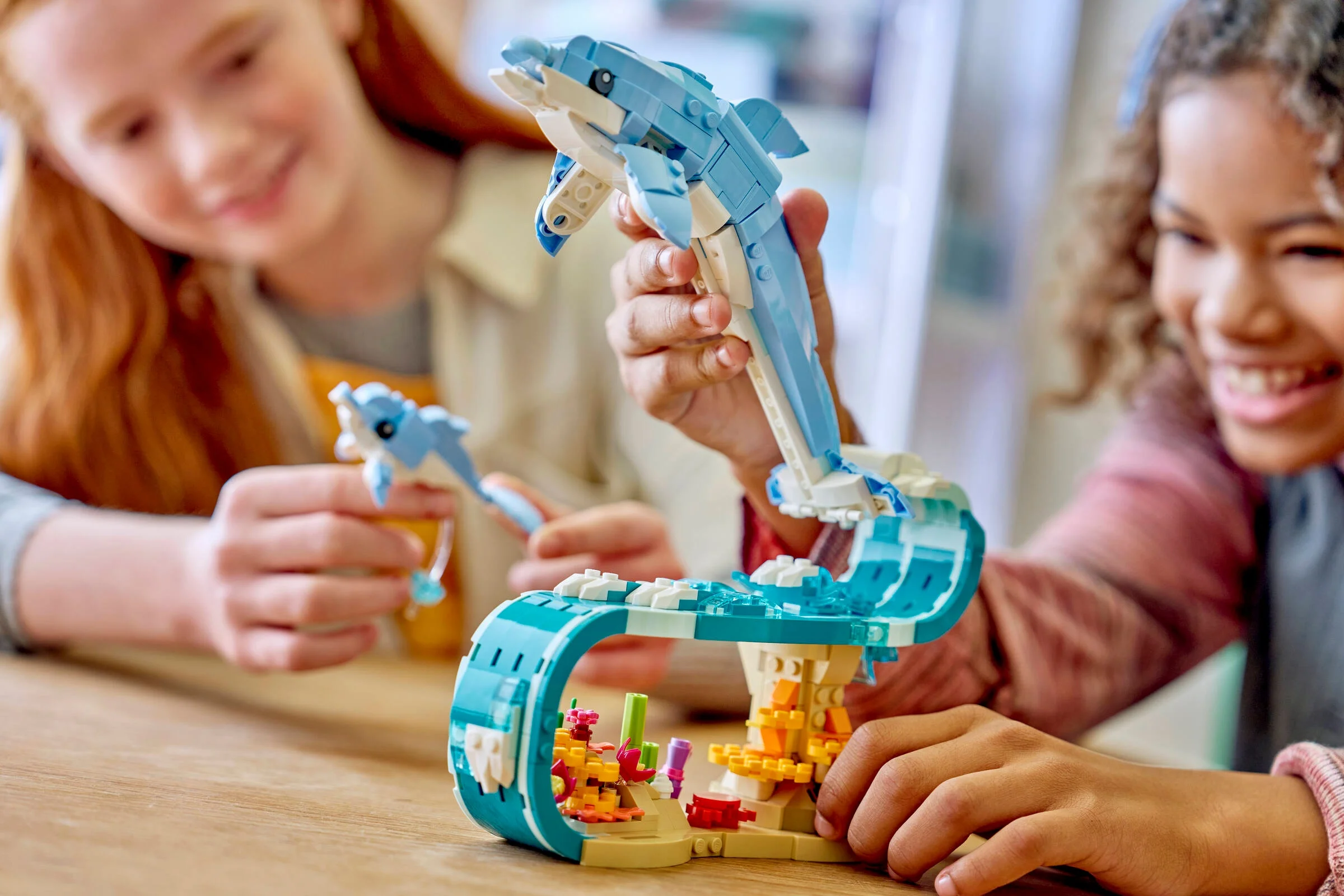 Două fete se joacă cu setul LEGO cu delfini, prezentând modelul asamblat.