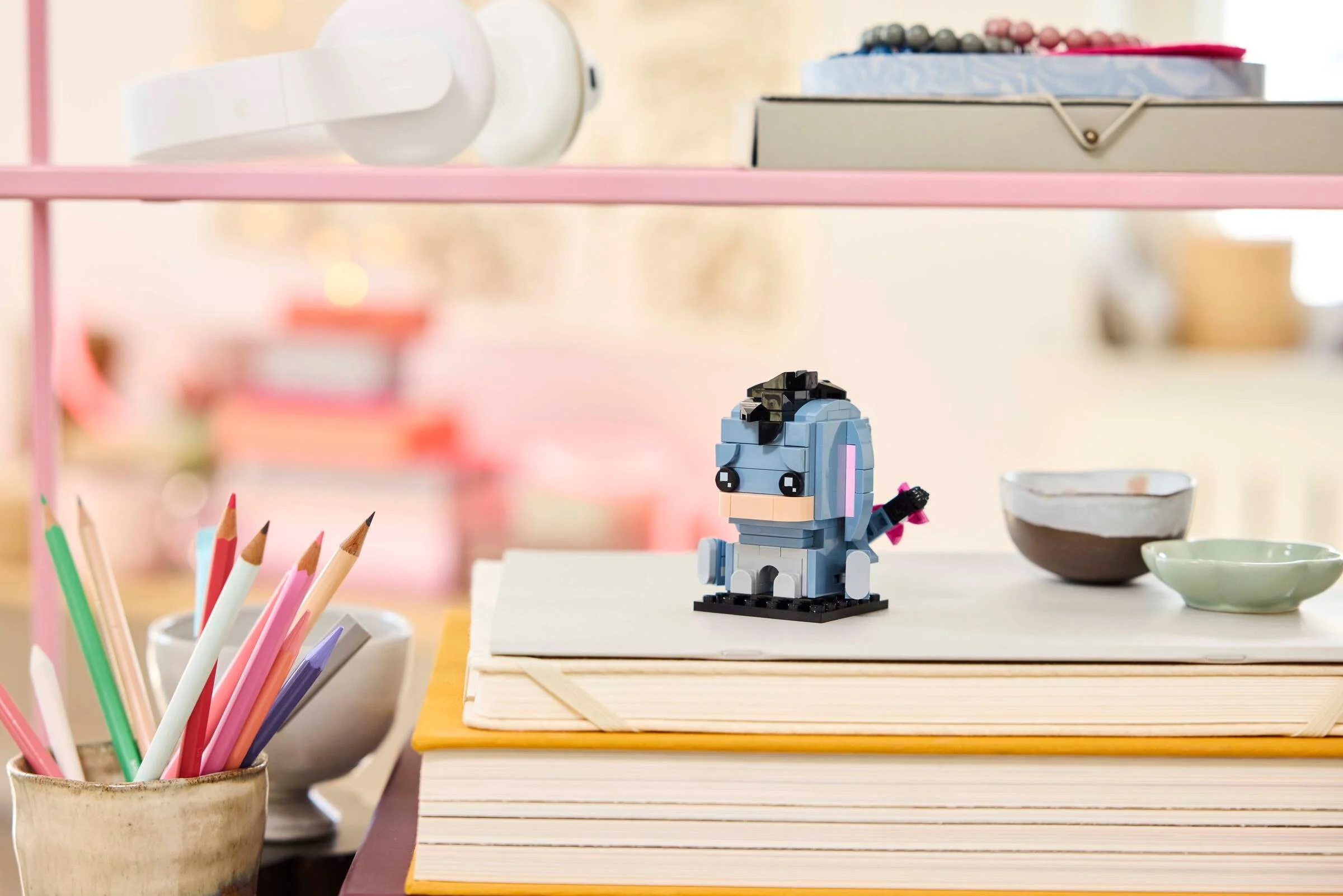 Eeyore BrickHeadz pe o stivă de cărți, decor creativ. Detaliu simpatic și colorat.