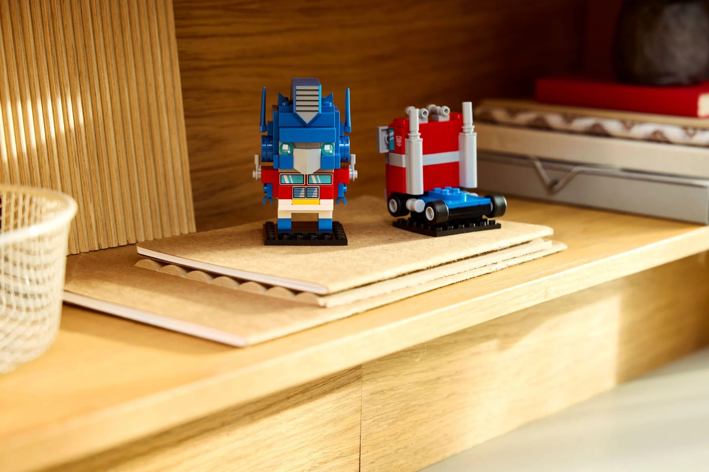 Imagine cu modelul BrickHeadz Optimus Prime robot și camion pe un raft de lemn.
