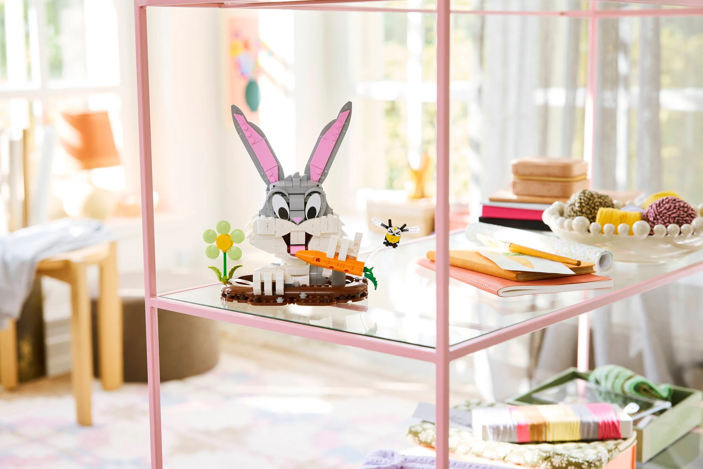 Modelul LEGO Bugs Bunny stă pe un raft roz de sticlă, cu un morcov în mână.