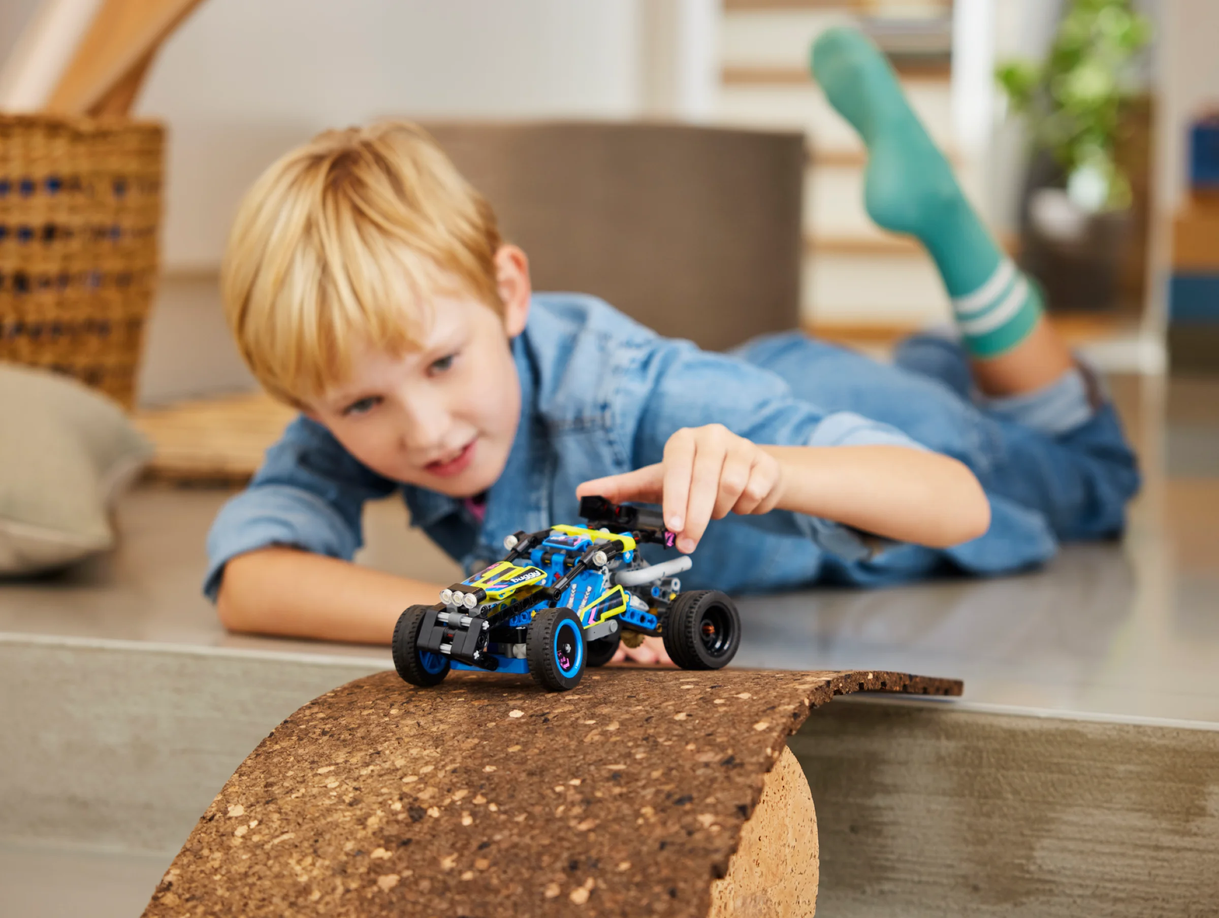 Un băiat se joacă cu buggy-ul Off-Road Race LEGO Technic, simulând o cursă pe o rampă mică.