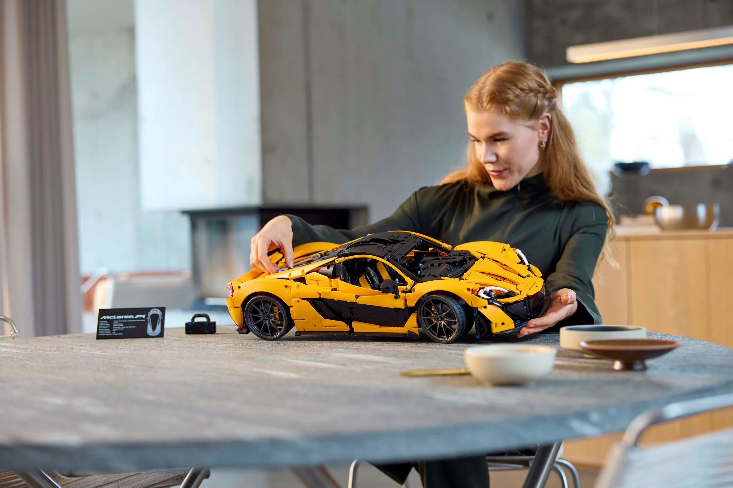 O femeie asamblează mașina McLaren P1 LEGO Technic. Model detaliat, galben cu negru.