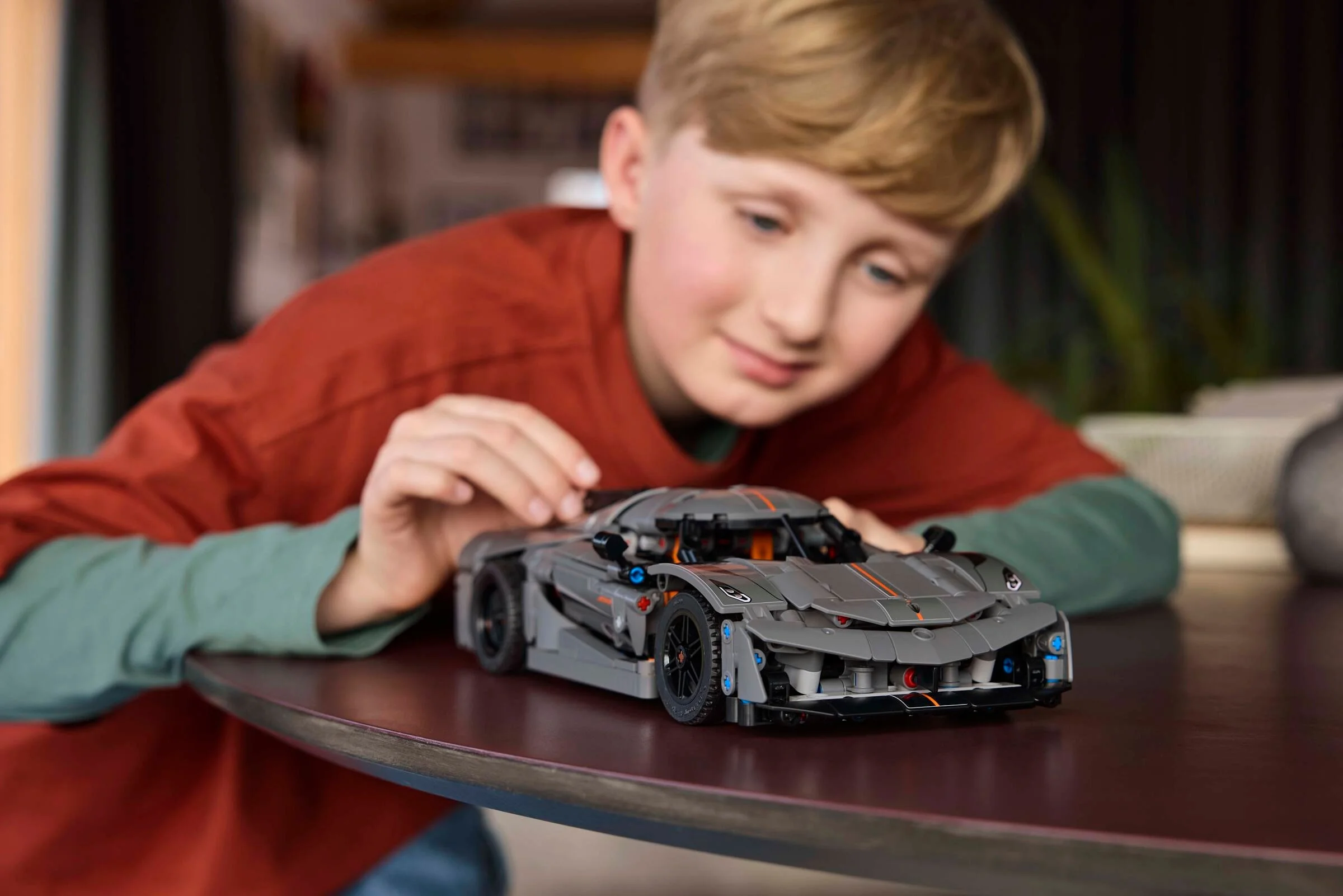 Un băiat admiră modelul LEGO Technic Koenigsegg Jesko Absolut gri pe o masă.
