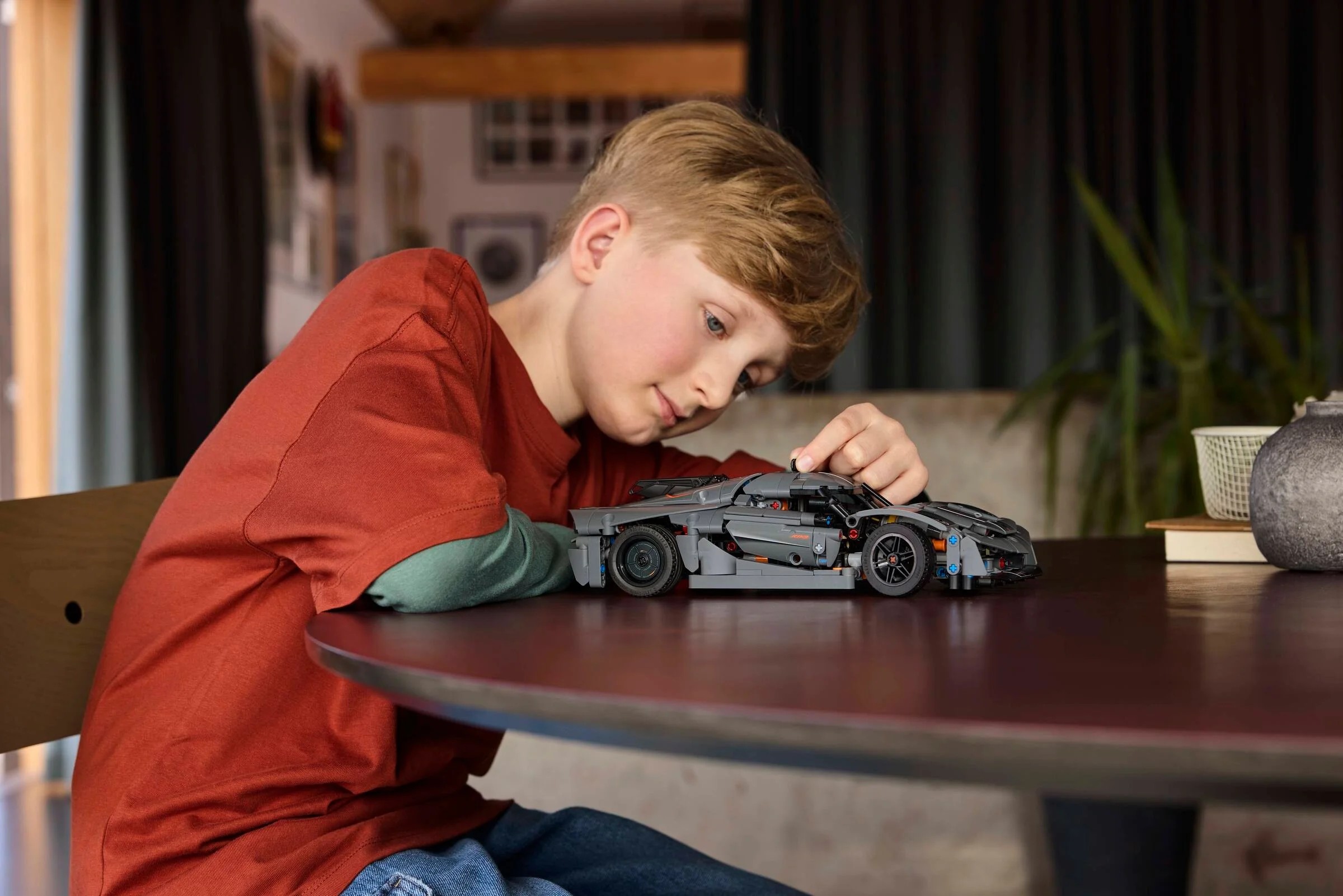 Un băiat explorează modelul LEGO Technic Koenigsegg Jesko Absolut gri. Detaliile mașinii sunt vizibile.
