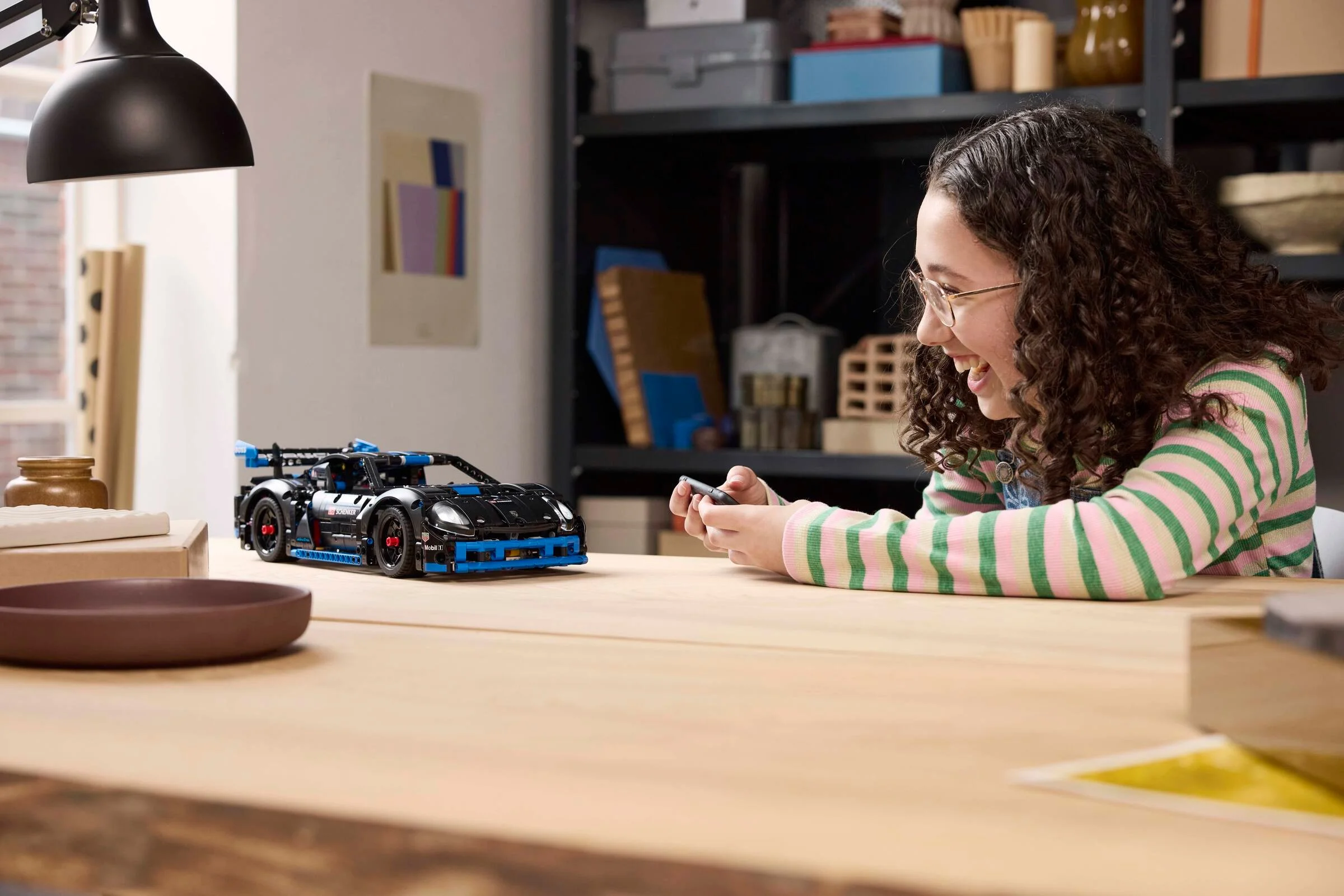 Fată zâmbitoare controlează mașina de curse Porsche GT4 e-Performance LEGO Technic.