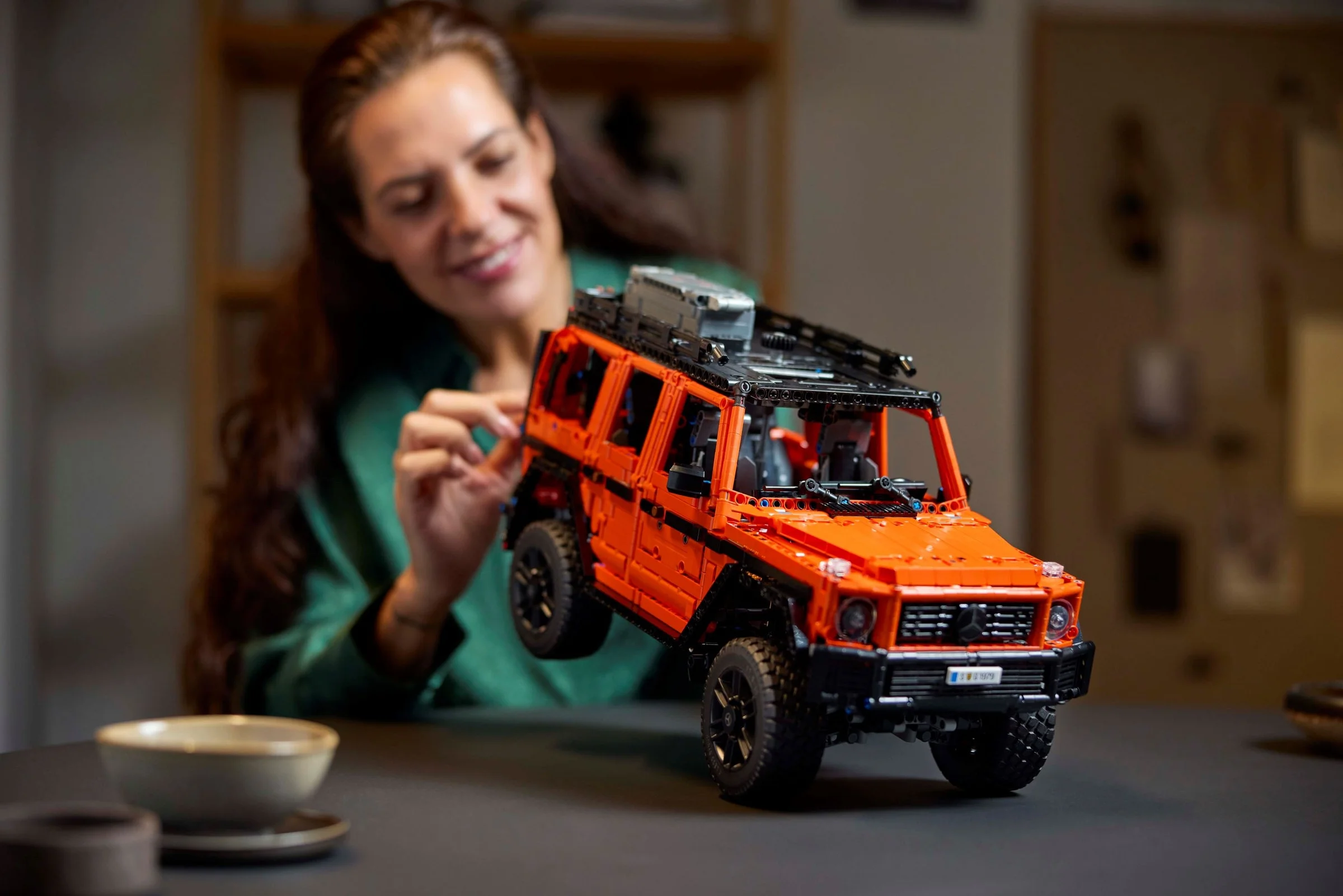 Femeie interacționând cu modelul LEGO Mercedes-Benz G 500, portocaliu, pe o masă.