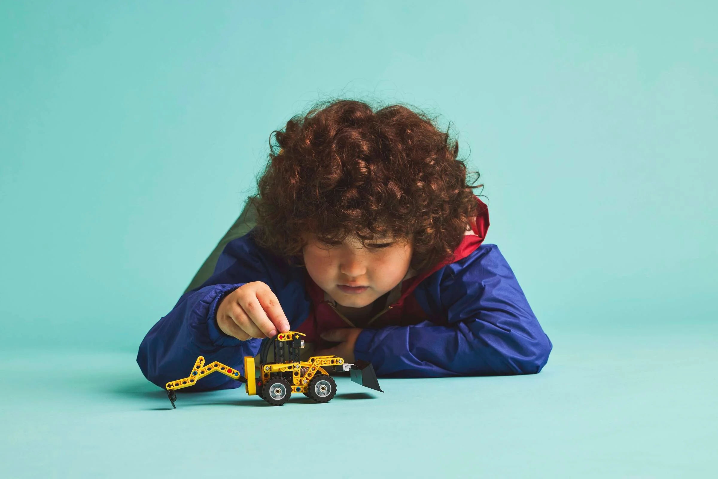 Băiat concentrat jucându-se cu modelul LEGO Technic al încărcătorului spate. Joacă creativă.