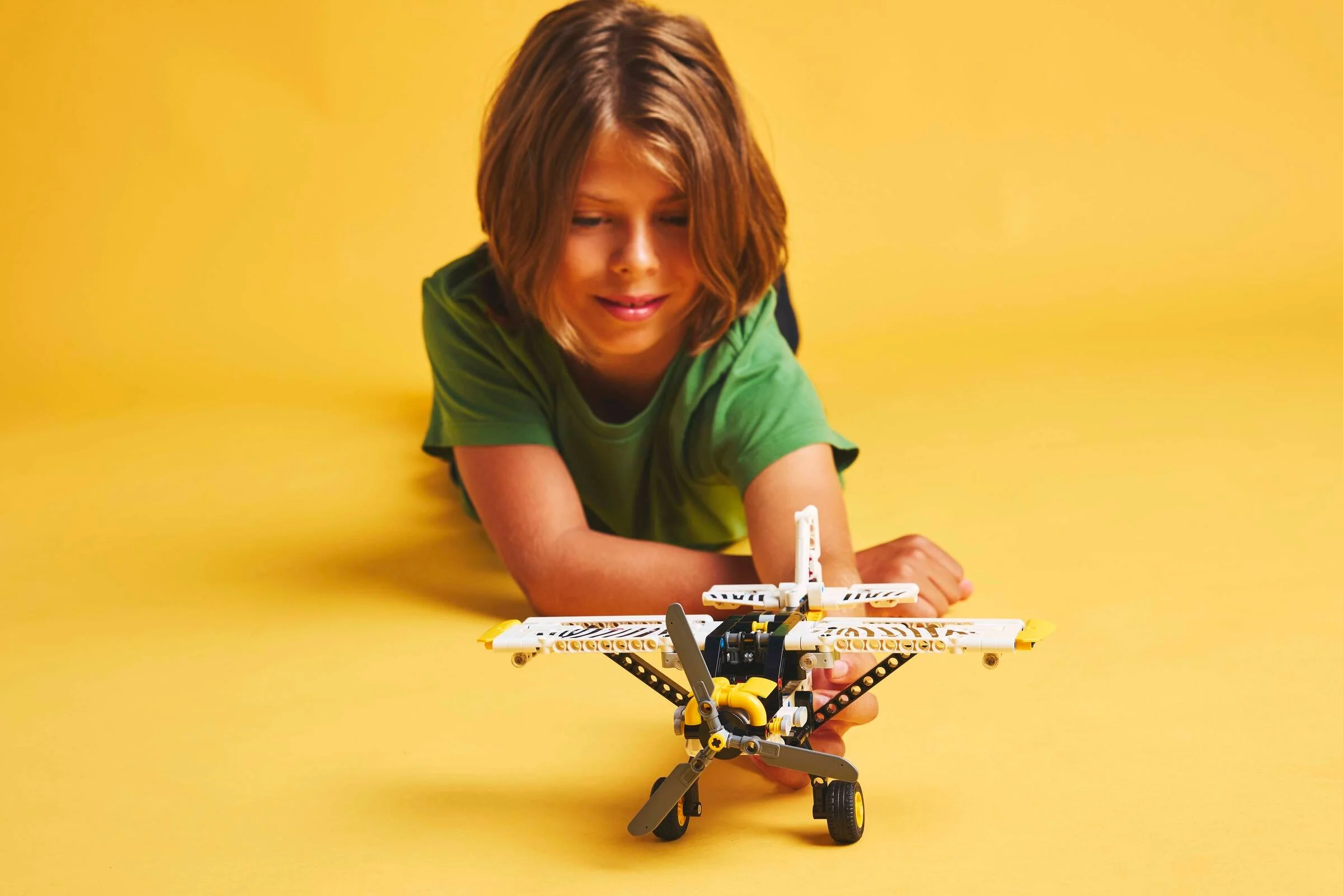 Copil se joacă cu avionul de tufiș LEGO Technic 42198 pe un fundal galben.