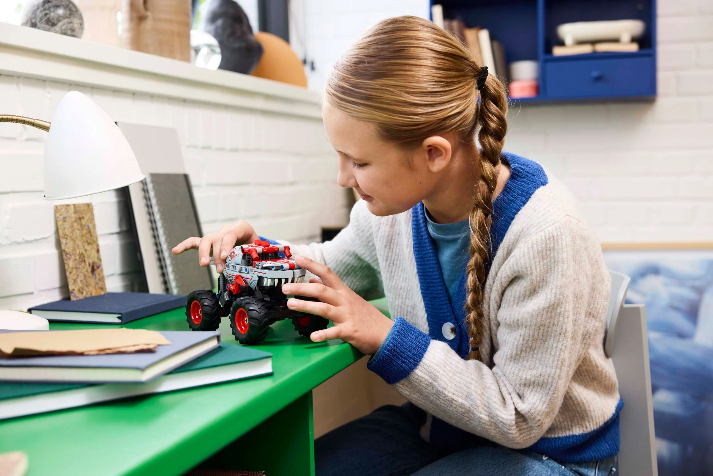 Fată se joacă cu ThunderROARus LEGO Technic, pe un birou verde. Zâmbește și pare entuziasmată.