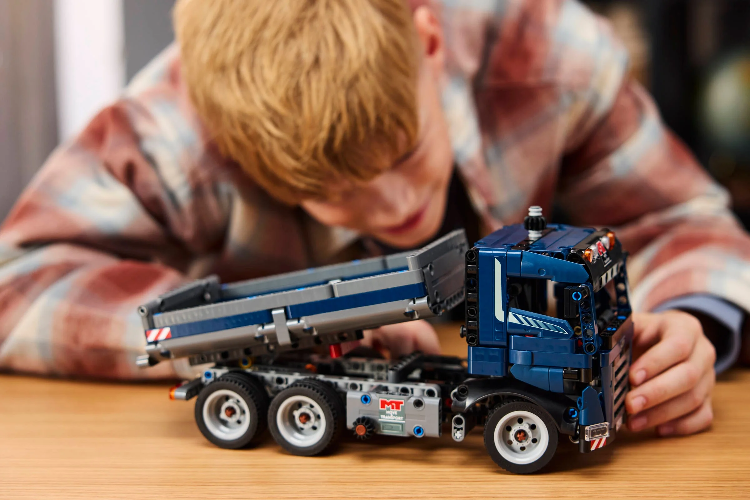 Băiat se joacă cu camionul basculant din LEGO Technic, bena fiind ridicată.