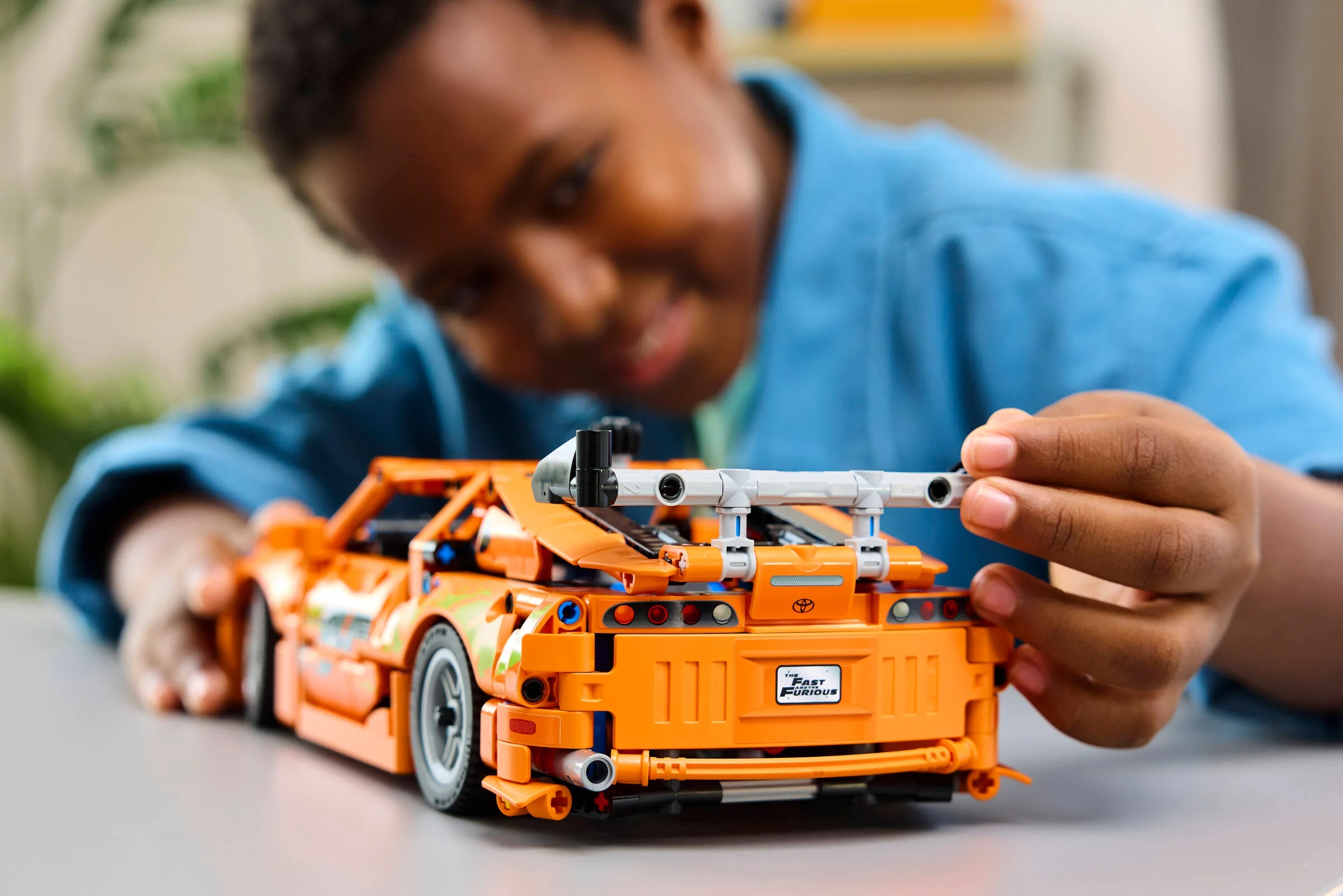 Copil interacționând cu modelul LEGO Toyota Supra MK4, spate detaliat, portocaliu intens.