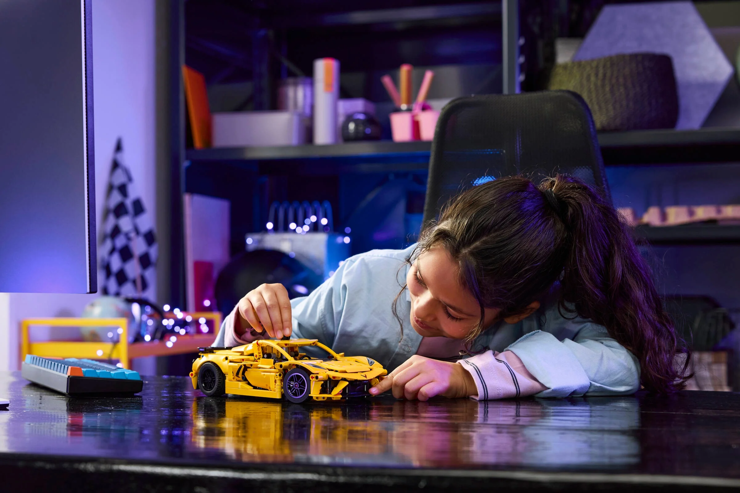 O fetiță construiește Corvette Stingray galben din LEGO Technic. Model detaliat, atractiv.