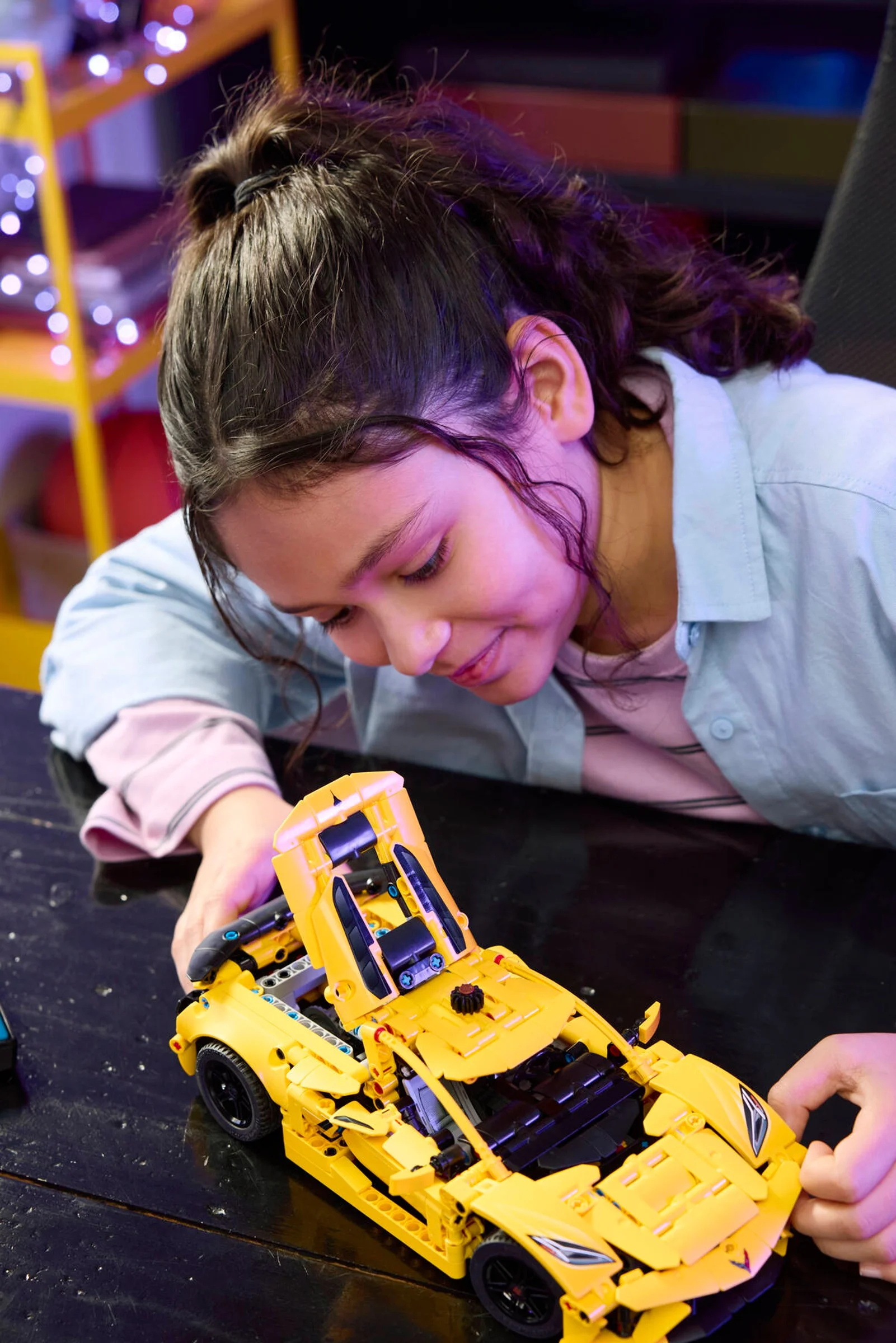 Fetiță zâmbitoare construind modelul LEGO Chevrolet Corvette Stingray galben.