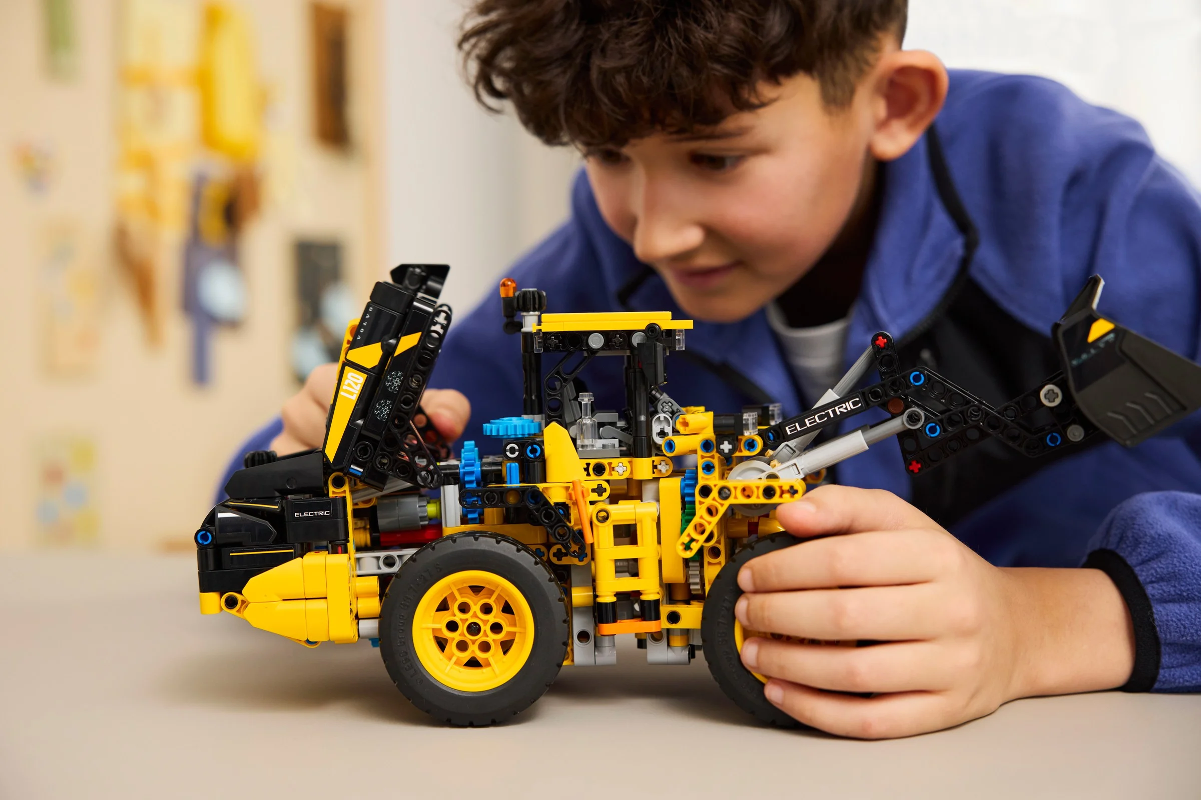 Băiat se joacă cu Volvo L120 Electric Wheel Loader, un model LEGO Technic galben și negru.
