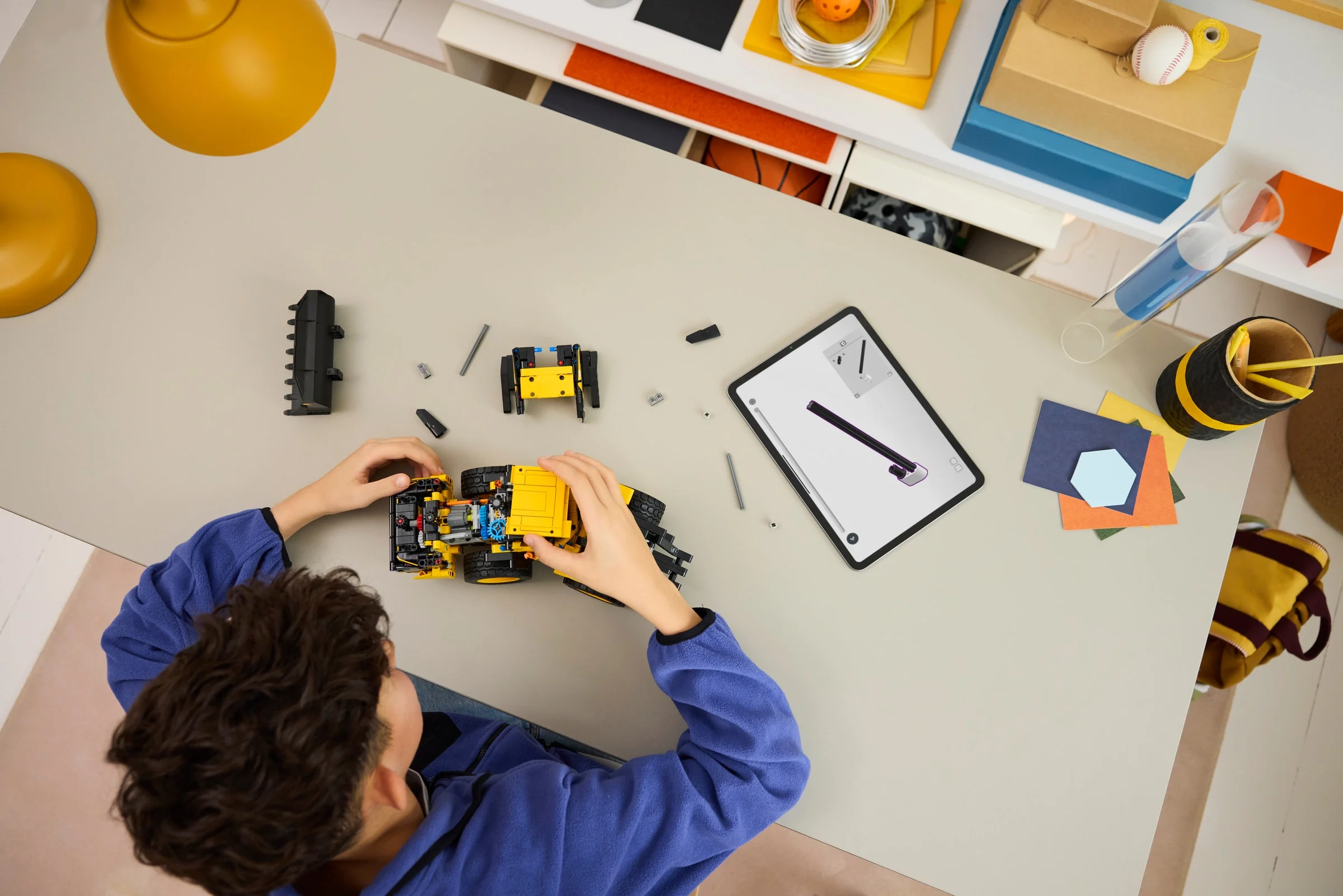 Copil construind modelul LEGO Volvo L120 după instrucțiuni digitale pe tabletă.